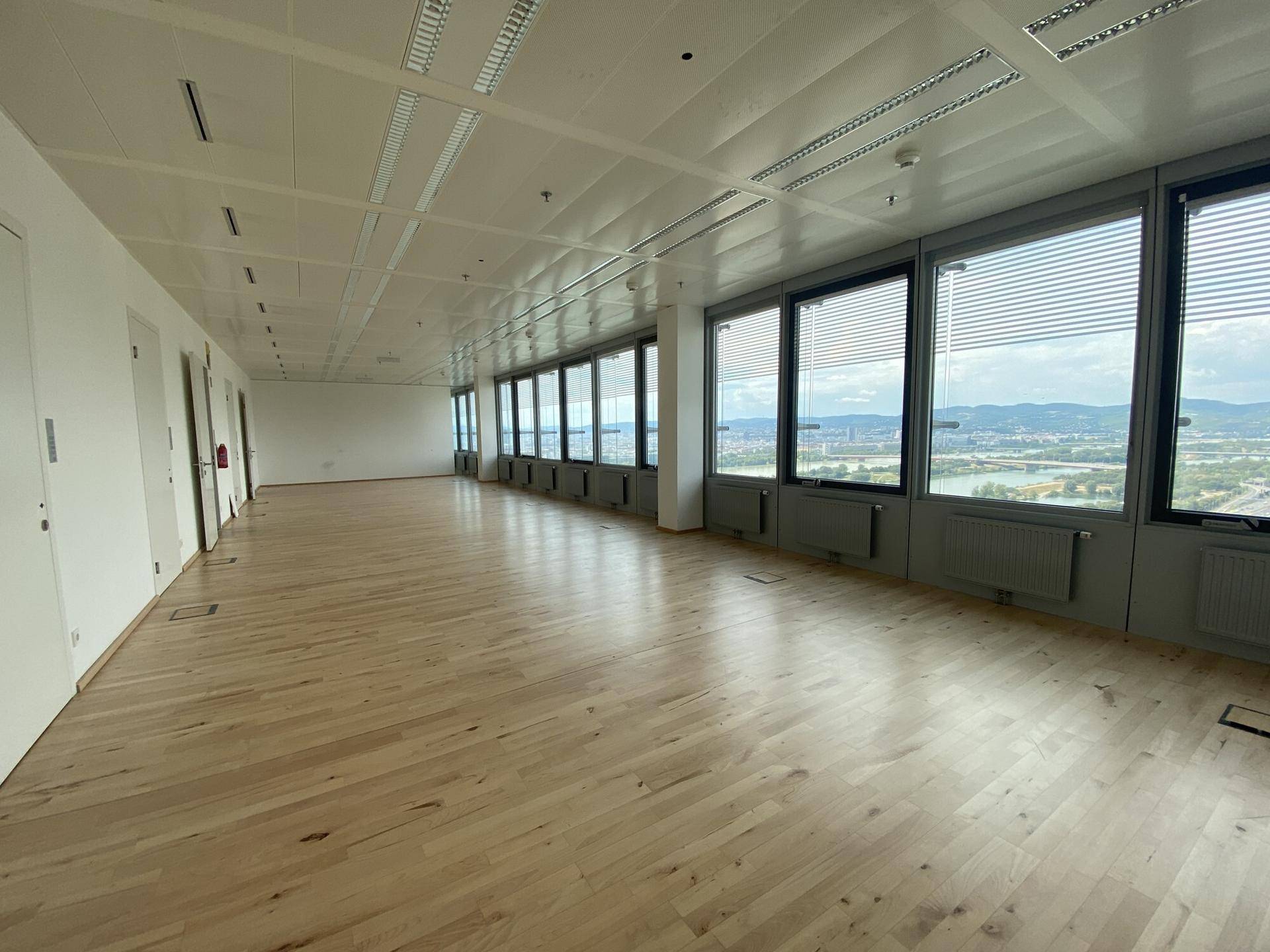 Geräumiger Bürobereich mit hellem Holzplankenboden und einer Fensterfront mit Panoramablick über die Stadt.