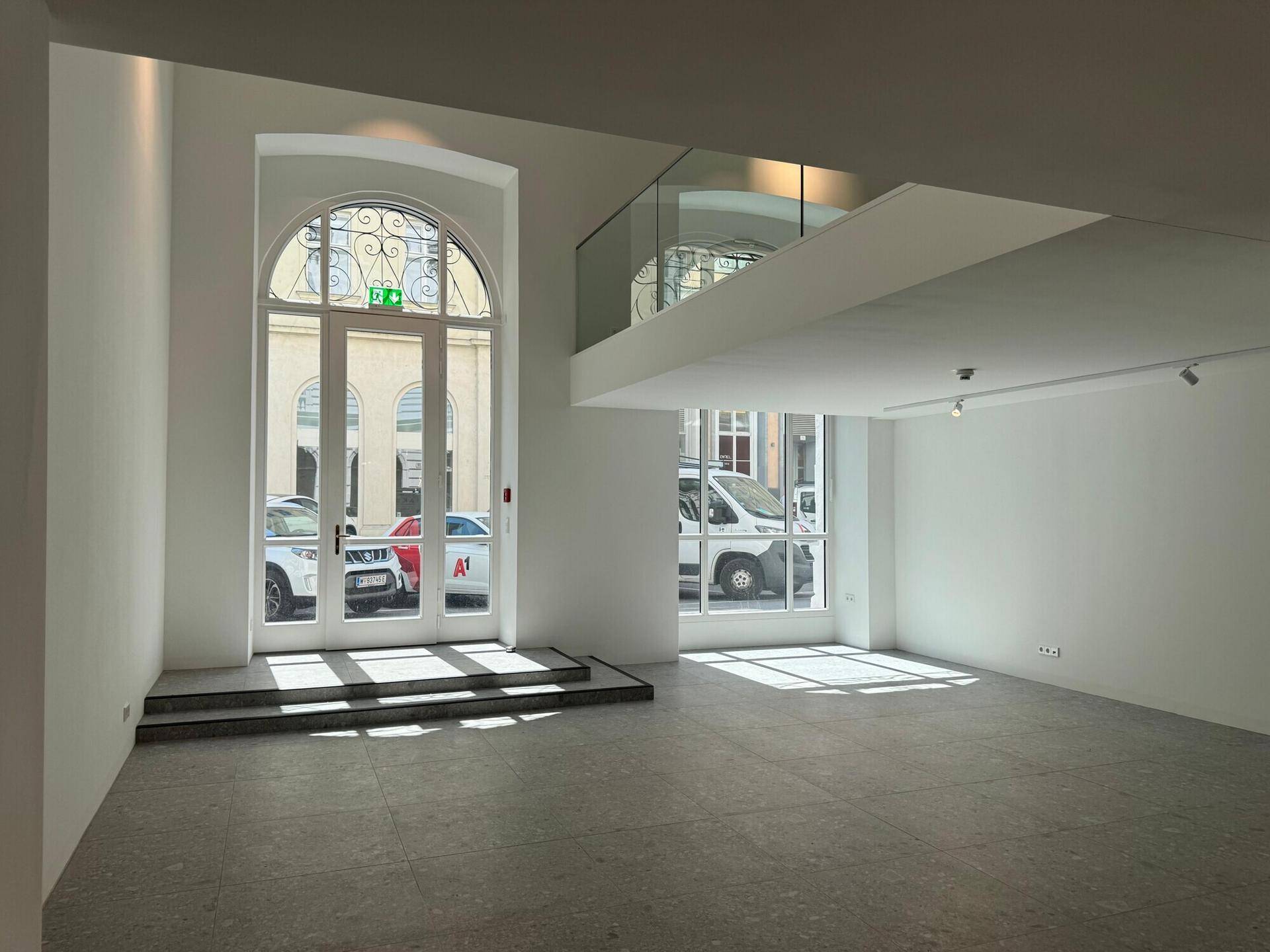 Heller, offener Gewerberaum im Erdgeschoss mit hohen Decken, großen Fenstern und einer modernen Galerie mit Glasgeländer.