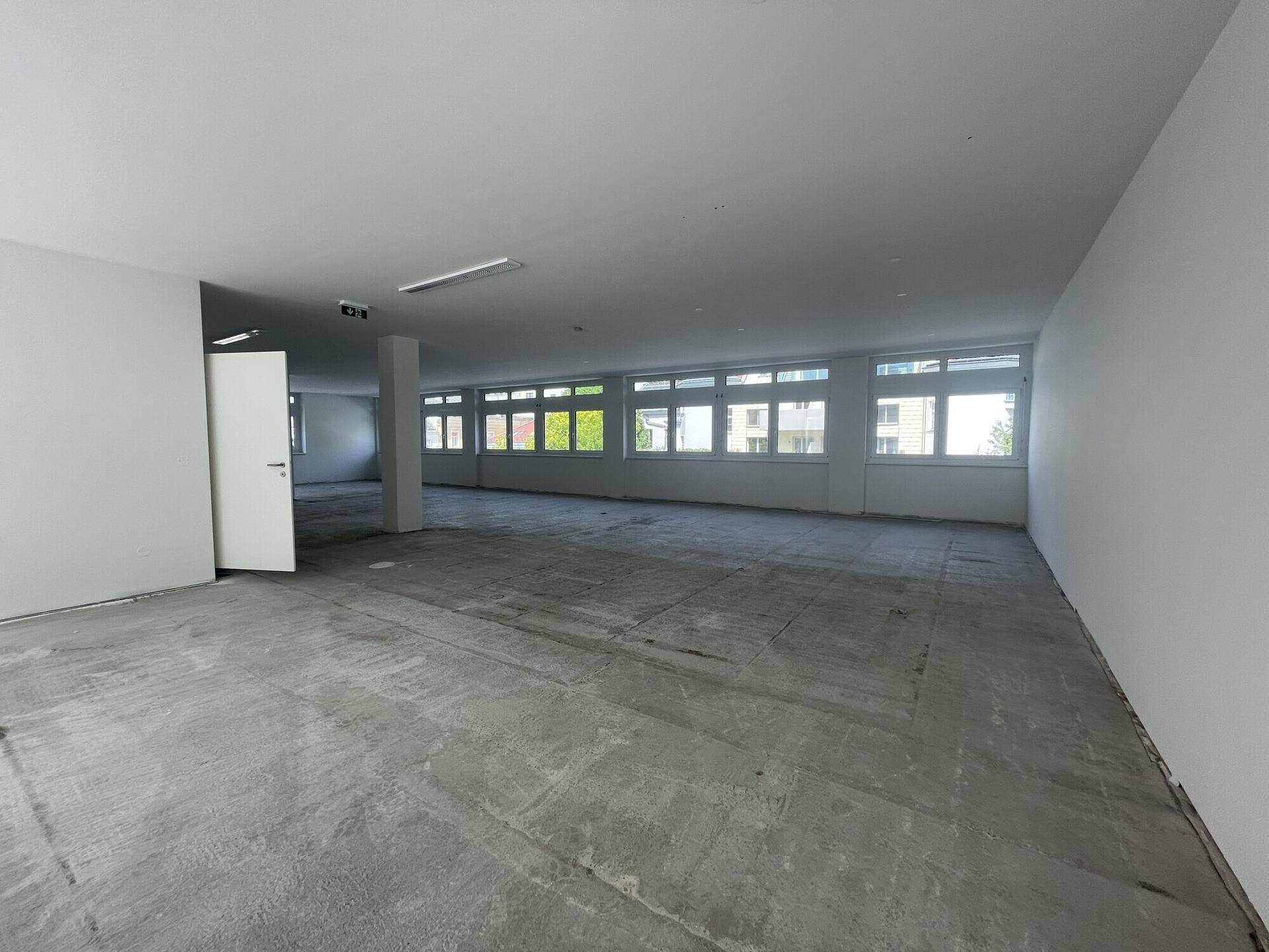 Geräumiger, heller Büroraum im Rohbau mit vielen Fenstern und einer offenen Gestaltung.