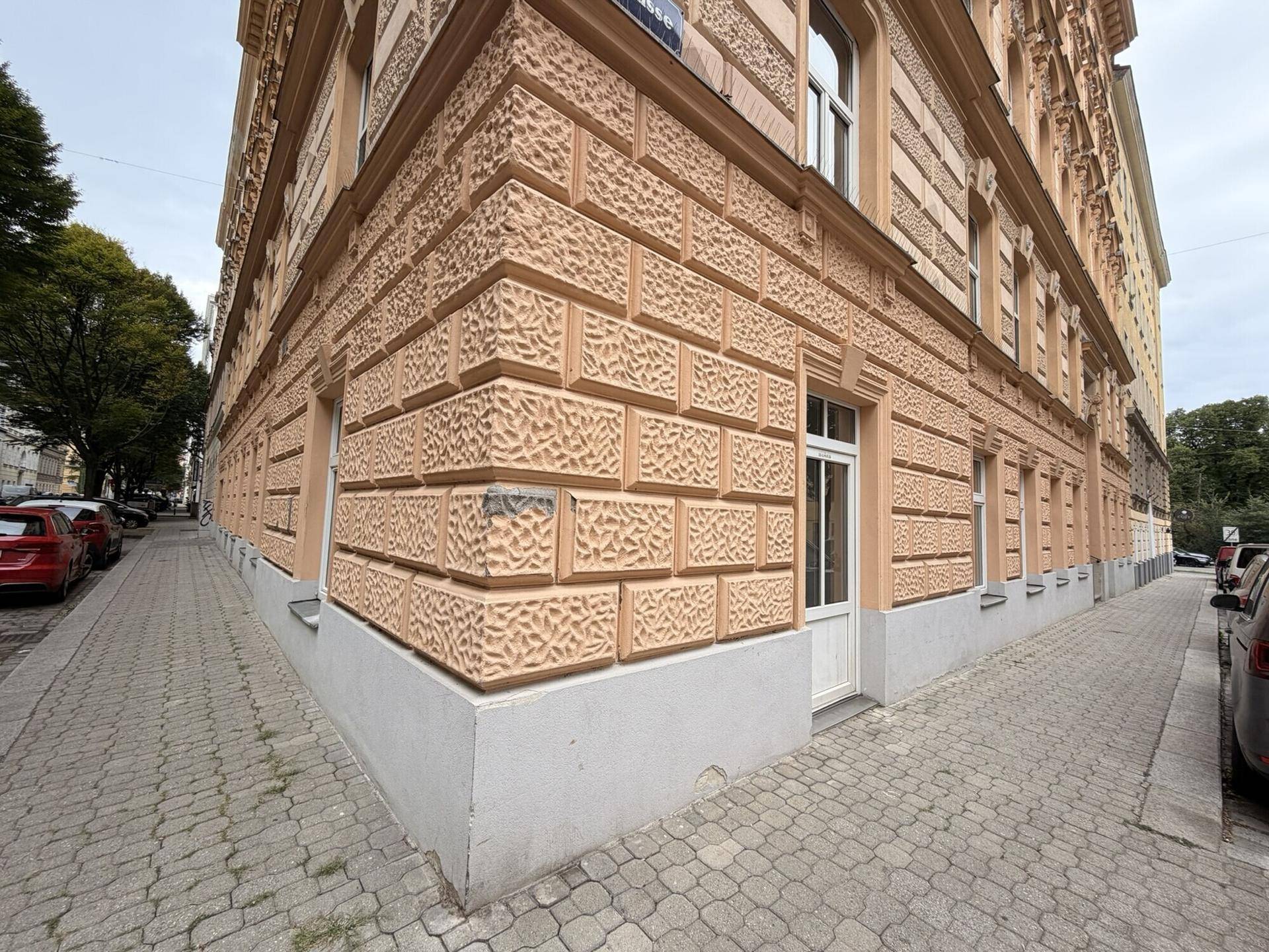 Detailansicht der Gebäudeecke mit strukturierter Fassade und einem Eingang im Erdgeschoss.