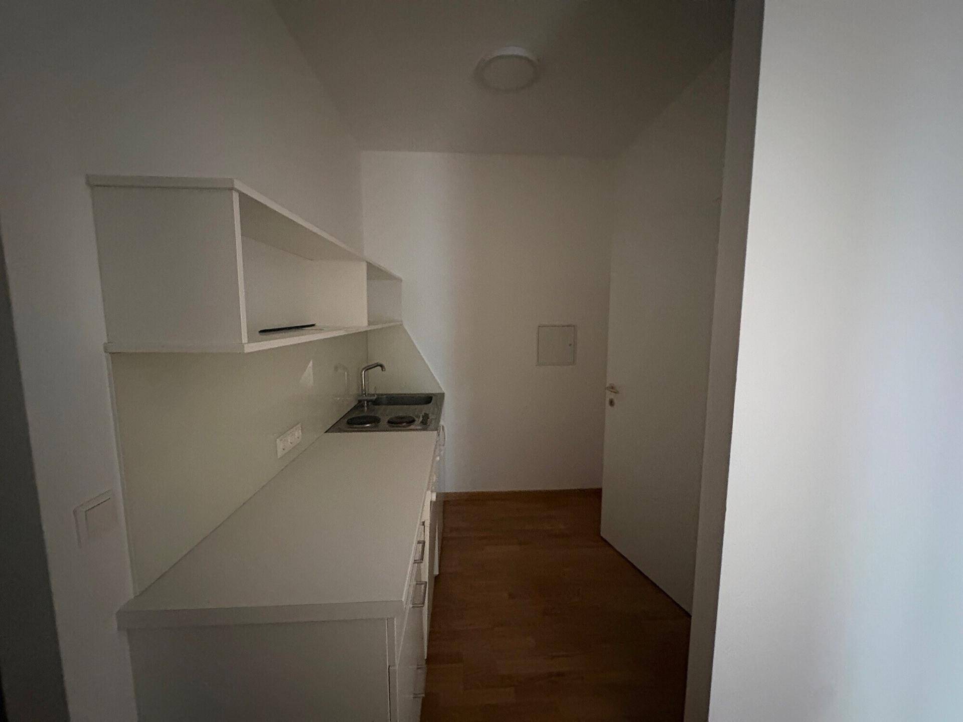 Moderne Küchenzeile mit weißen Schränken, Spüle und Kochfeld in einem kompakten Raum.
