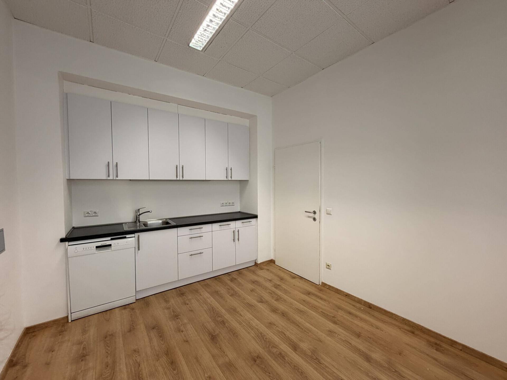 Moderne Küchenzeile mit weißen Schränken, schwarzer Arbeitsplatte und integriertem Geschirrspüler.