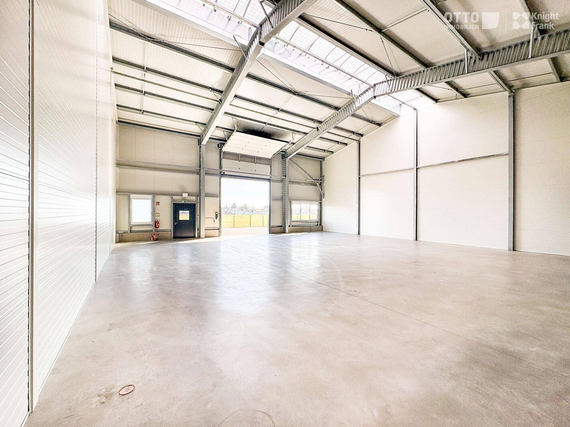 Geräumige, leere Lagerhalle mit hohen Decken, Betonboden und Oberlichtern für viel Tageslicht.