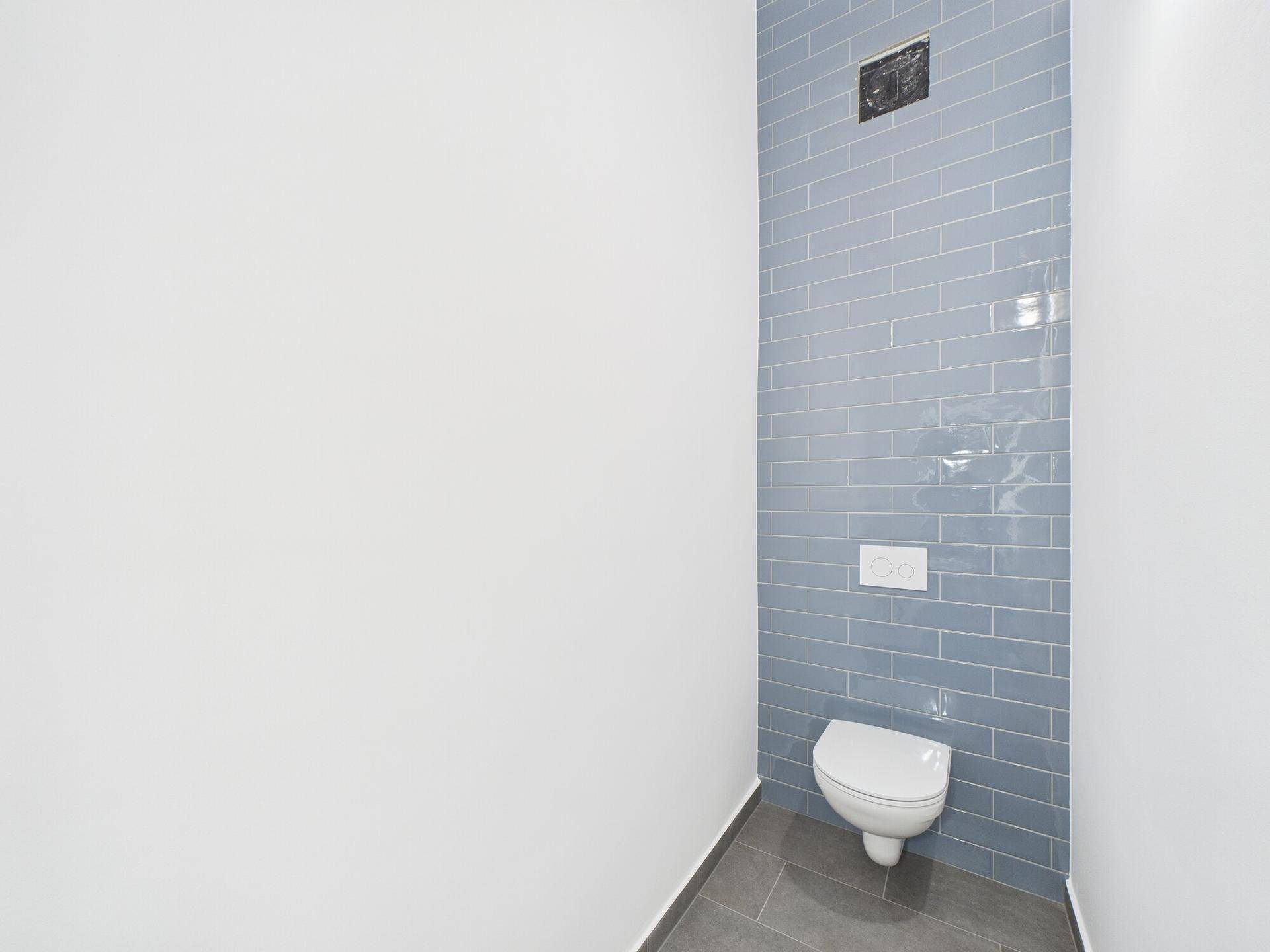 Modernes WC mit wandhängender Toilette und stilvollen blauen Fliesen an einer Akzentwand.