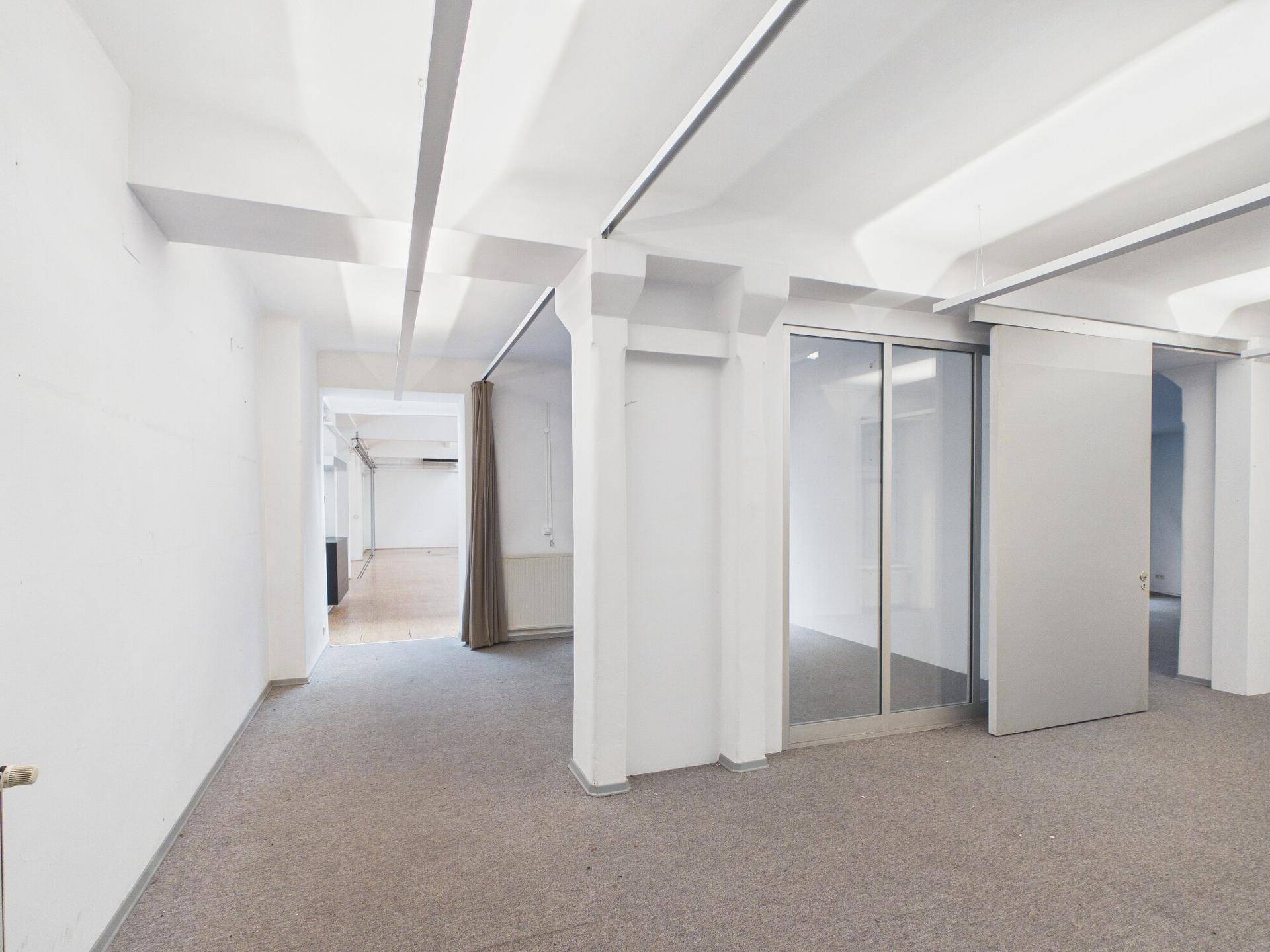 Moderner Bürobereich mit grauem Teppichboden und flexiblen Glas-Schiebetüren, die den Raum unterteilen.