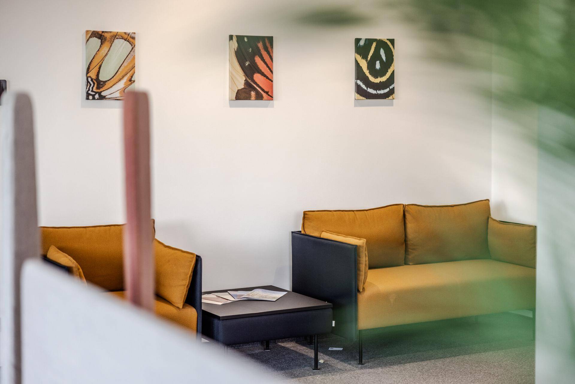 Gemütliche Lounge-Ecke im Büro mit bequemen gelben Sofas und dekorativen Bildern an der Wand.