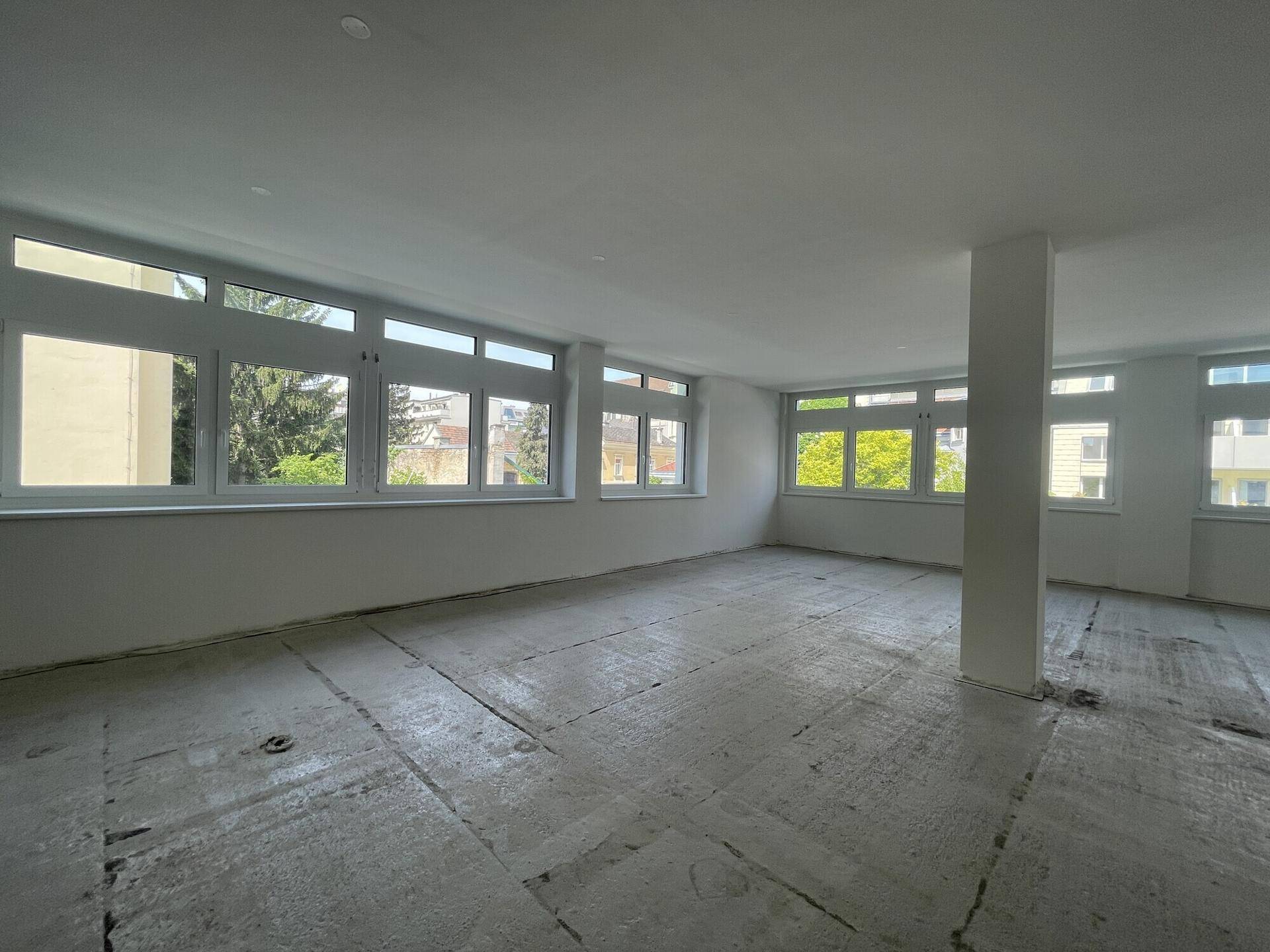 Großer, heller Büroraum im Rohbauzustand mit vielen Fenstern und Blick ins Grüne.