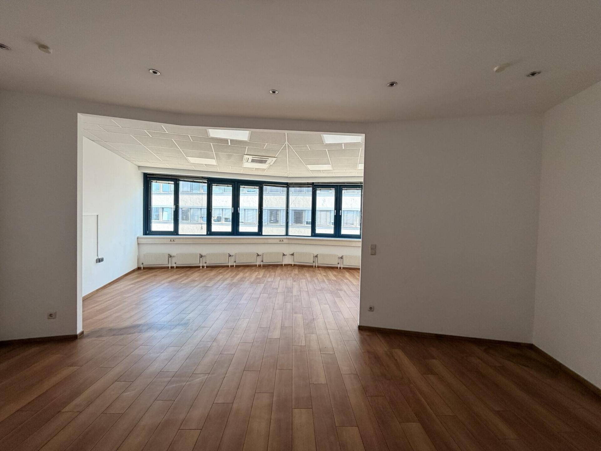 Großer Büroraum mit gebogener Fensterfront und Holzboden, bietet viel Tageslicht.