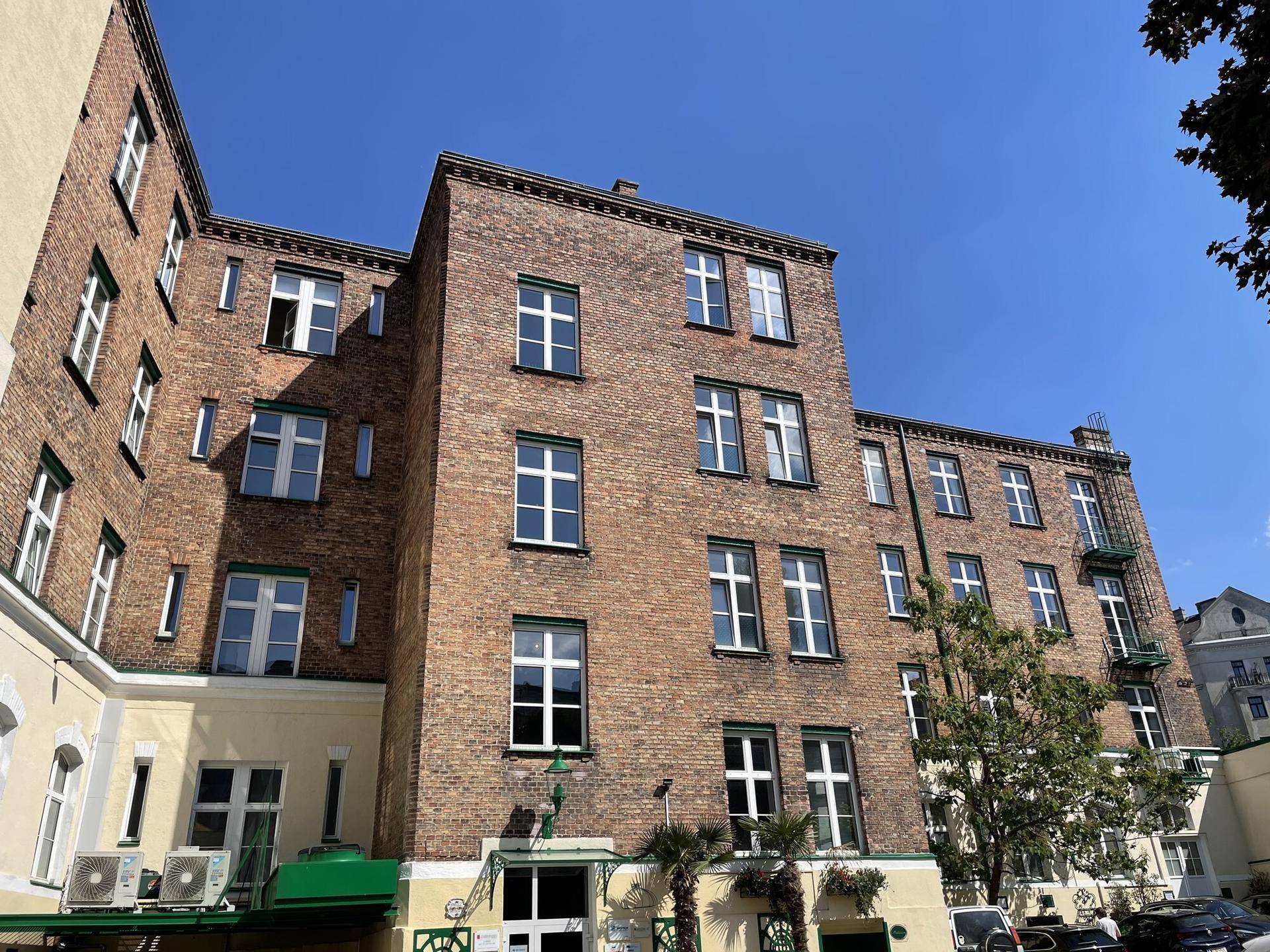 Historisches Backsteingebäude mit vielen Fenstern und sichtbaren Klimaanlagen in einem Innenhof.