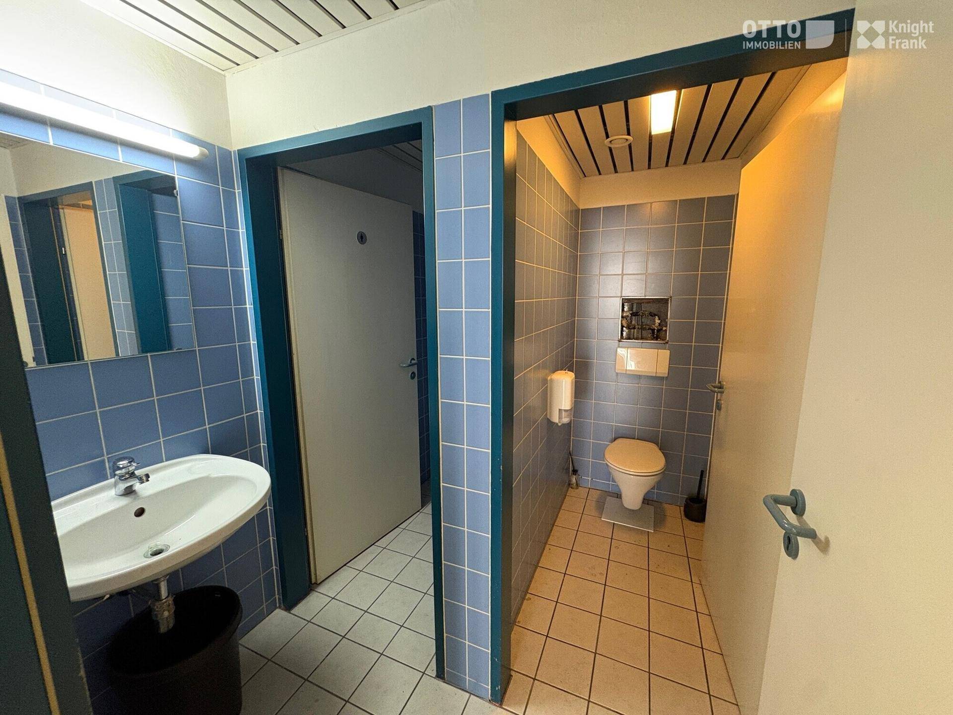 Sanitärbereich mit blauen Fliesen, Waschbecken und separater Toilette, funktional und sauber.