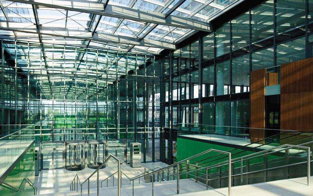 Weitläufiges Atrium mit Glasdach und Glasfassaden, das viel Tageslicht hereinlässt und eine offene Atmosphäre schafft.