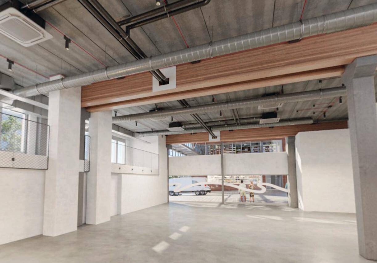 Weitläufiger, leerer Innenraum mit Betonboden, sichtbaren Lüftungsrohren und Holzbalken an der Decke.