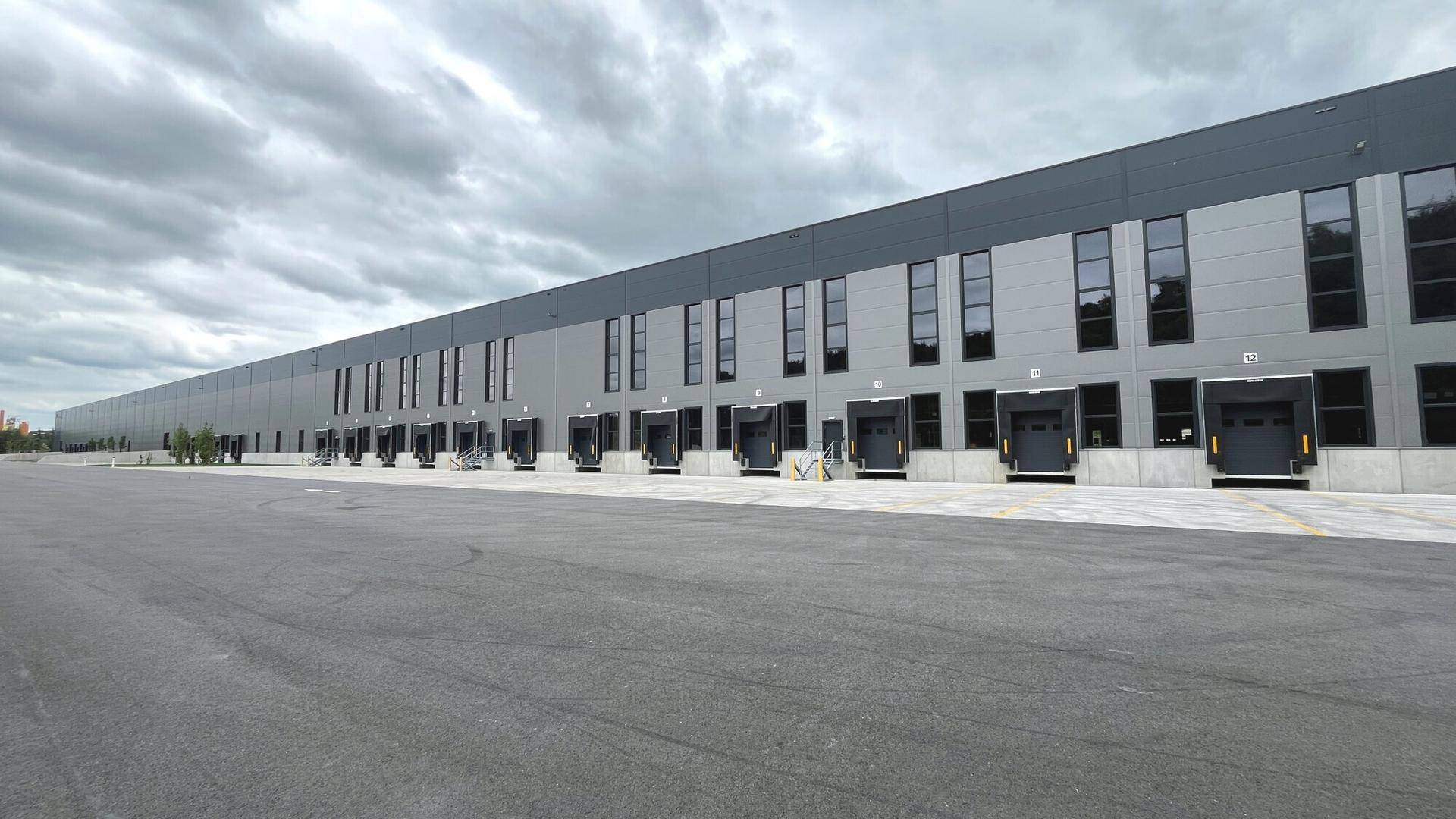 Lange, moderne Fassade eines Industriegebäudes mit zahlreichen Laderampen und großem asphaltierten Vorplatz.