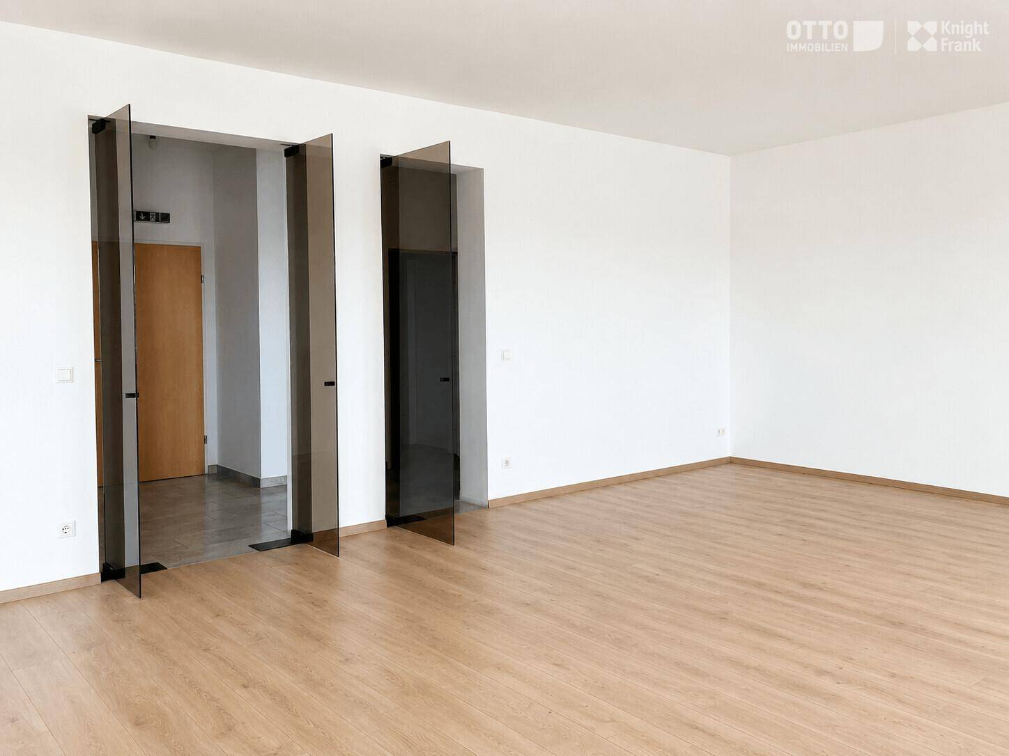 Heller Büroraum mit Laminatboden, weißen Wänden und modernen Glastüren.