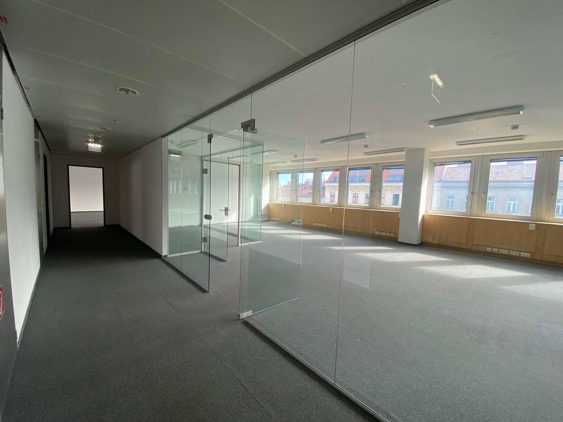 Geräumiges Büro mit Teppichboden, Glaswänden und Blick auf die Stadt durch die Fenster.