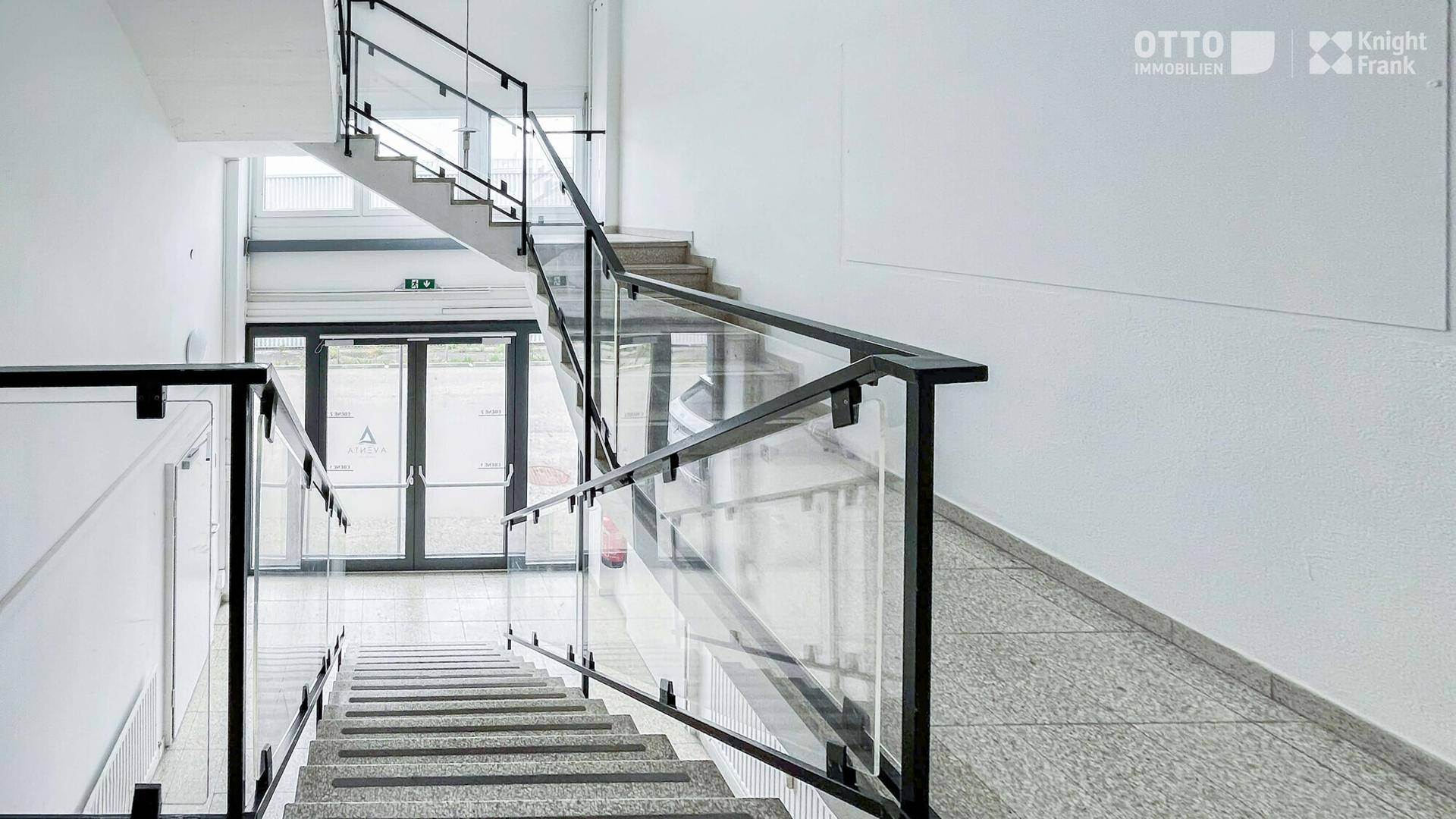 Modernes Treppenhaus mit Glasgeländer und Steinstufen, das zu den oberen Etagen führt.
