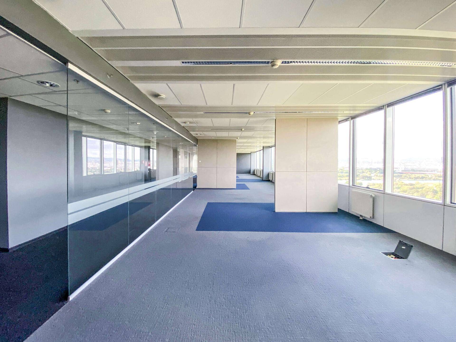 Moderner Bürobereich mit Glaswänden und Teppichboden, der einen weiten Blick auf die Stadt bietet.