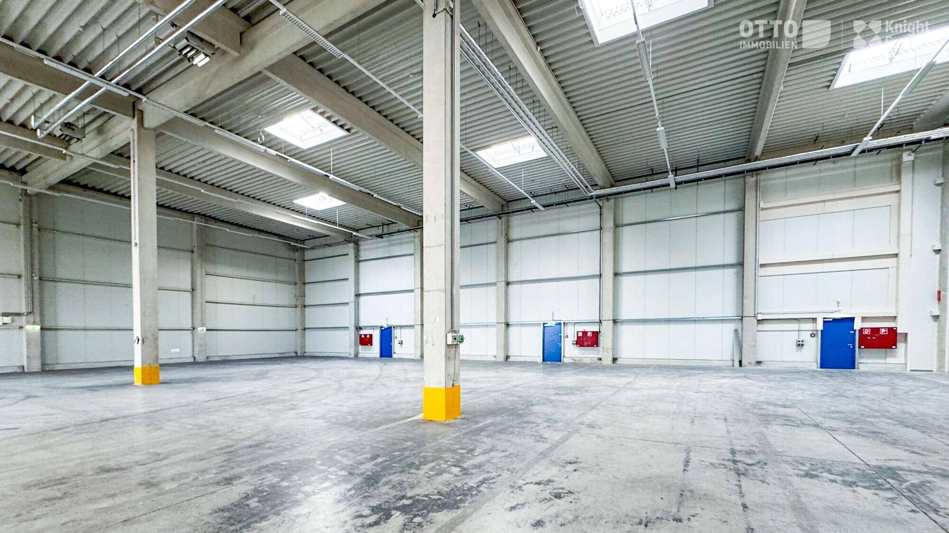 Weitläufige, leere Lagerhalle mit hohen Decken, Oberlichtern und Betonboden, bereit zur Nutzung.