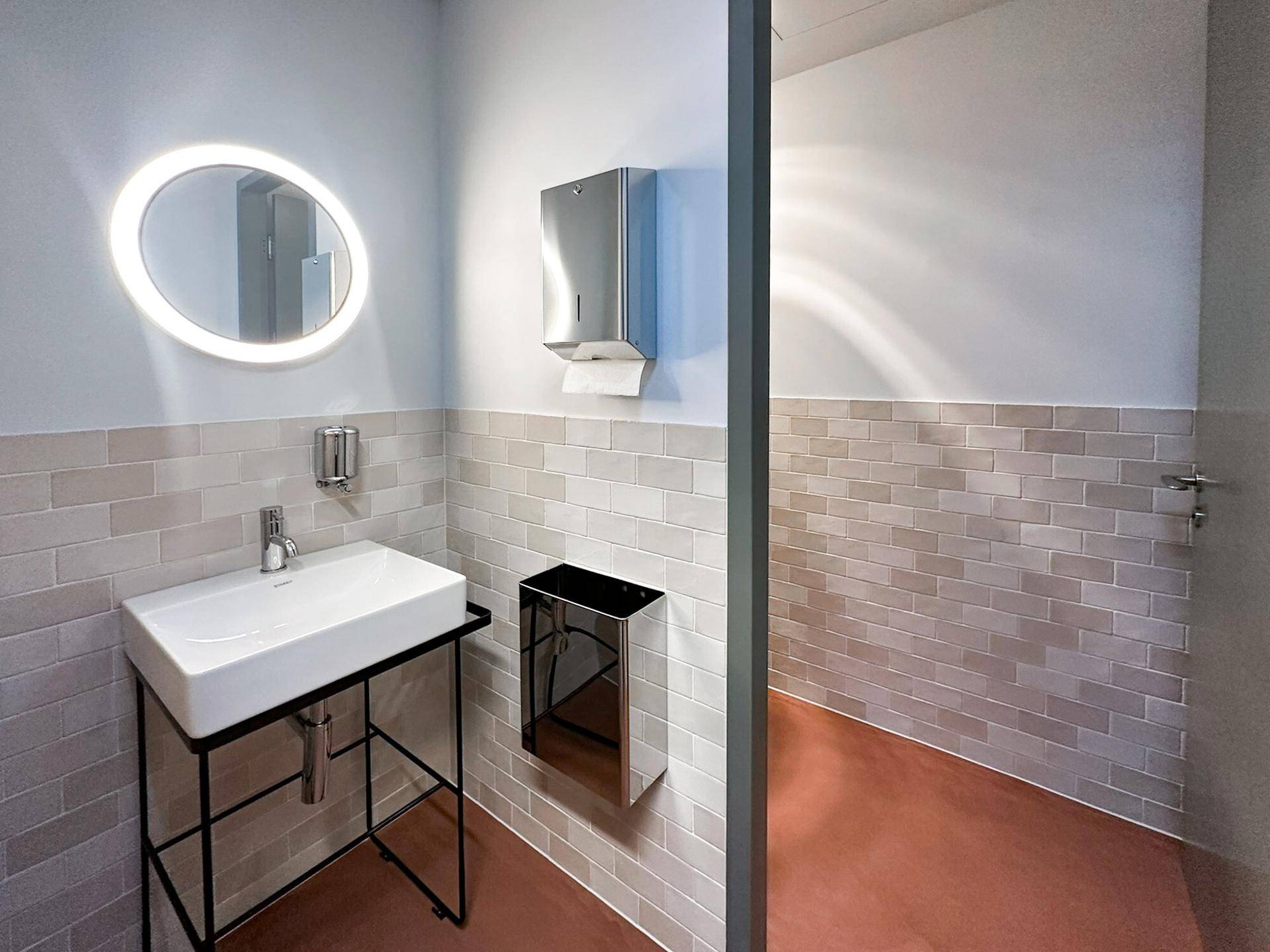 Modernes Badezimmer mit stilvollem Waschbecken, beleuchtetem Spiegel und hellen Fliesen, sehr gepflegt und funktional.