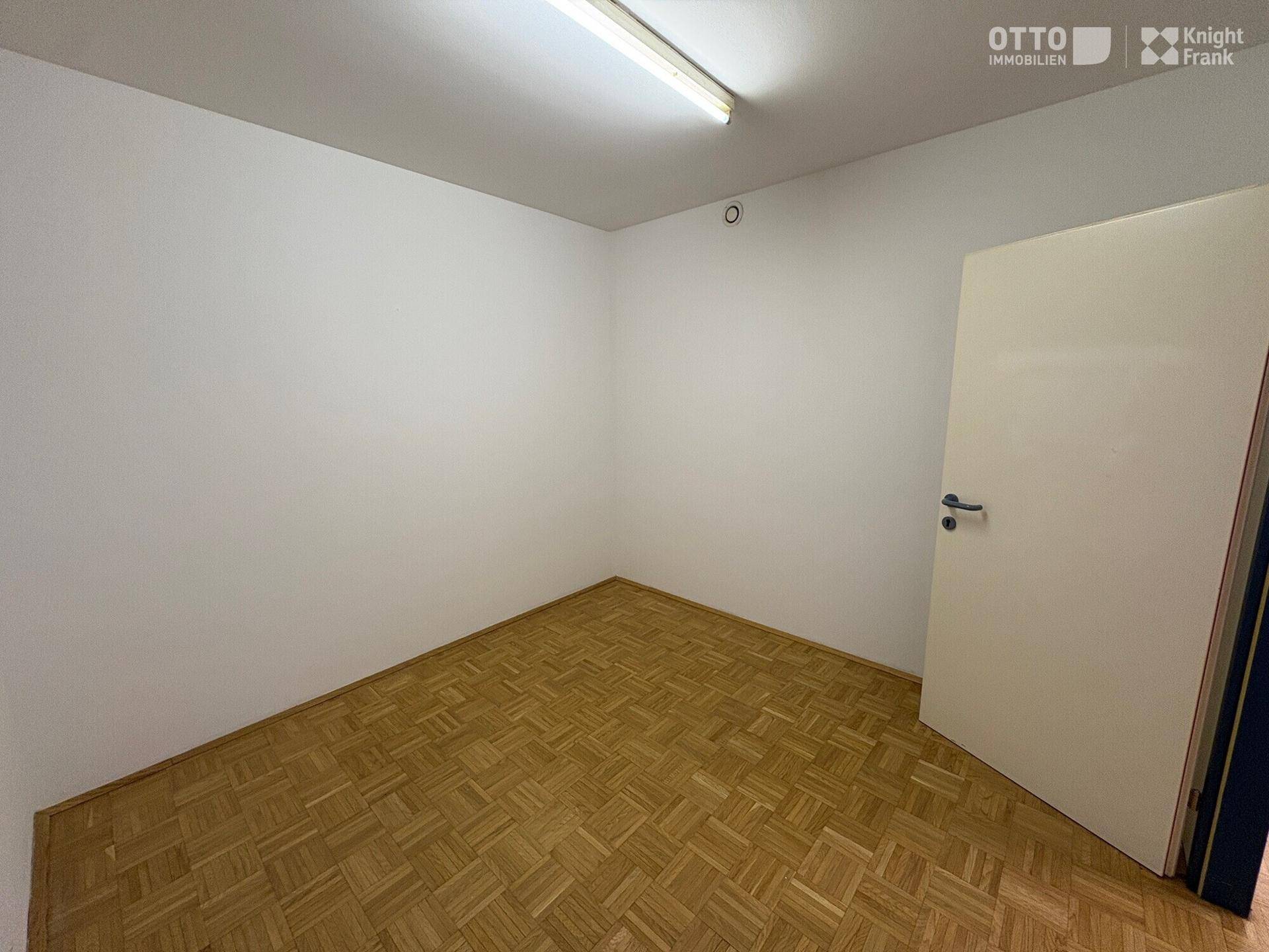 Kleiner, leerer Büroraum mit Parkettboden und weiß gestrichenen Wänden, bereit zur Nutzung.