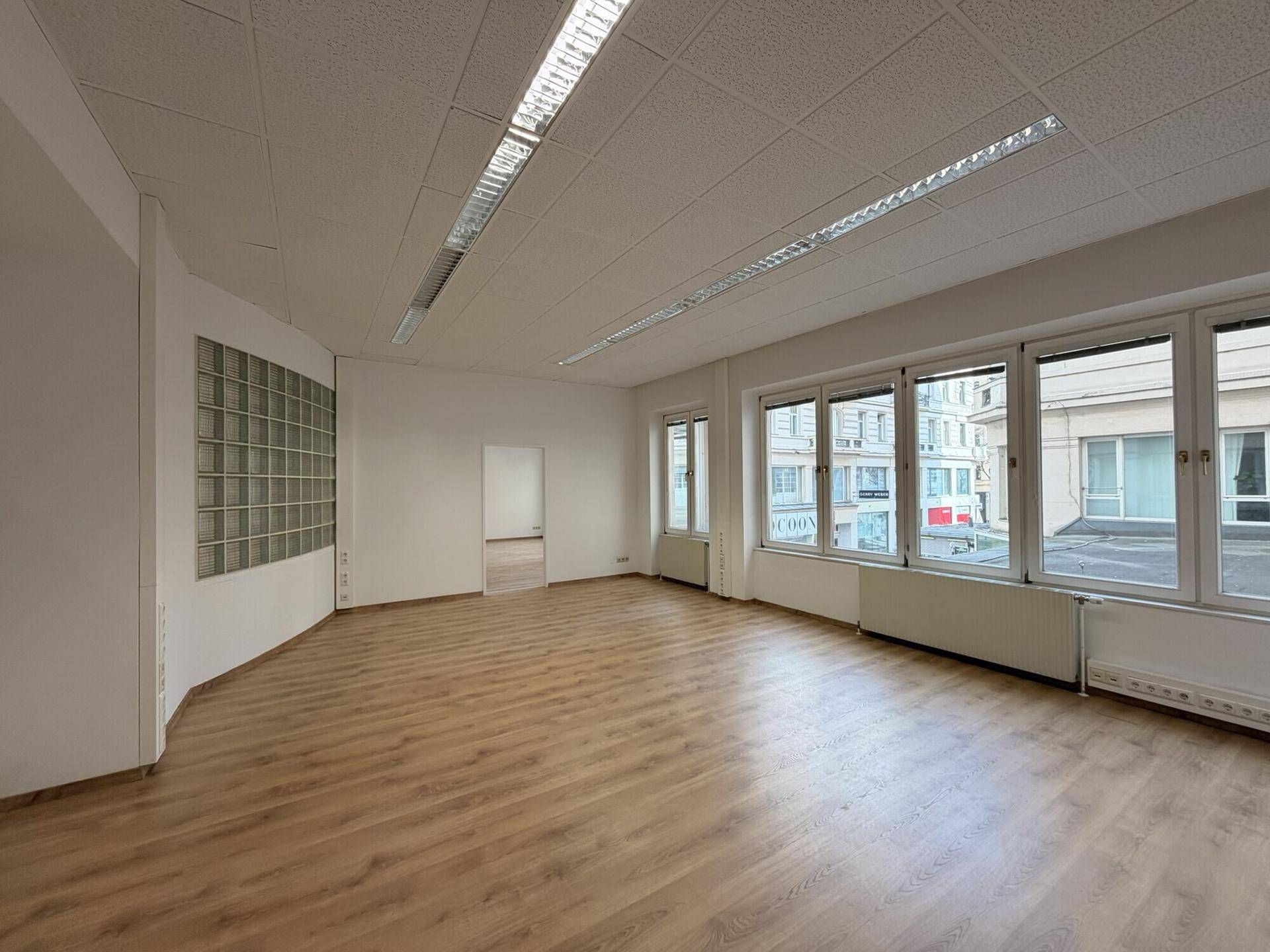Helles Büro mit Laminatboden, Glasbausteinwand und großen Fenstern mit Stadtblick.