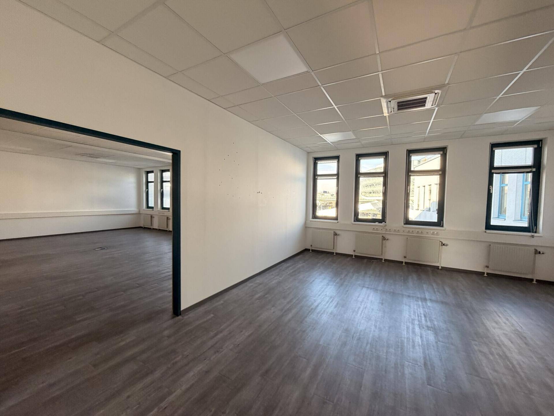 Leerer Büroraum mit dunklem Laminatboden und weißen Wänden, bereit zur Einrichtung.