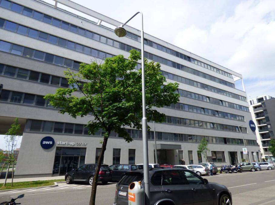 Ansicht des modernen Bürogebäudes von der Straße mit Bäumen und parkenden Autos im Vordergrund.