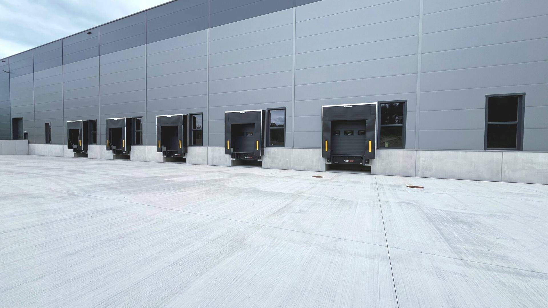 Reihe von Laderampen an der modernen Lagerhalle mit breiter Betonfläche für den Warenverkehr.