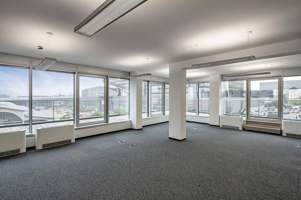 Geräumiges, leeres Büro mit großen Fenstern, Teppichboden und weitem Blick auf die Stadt.