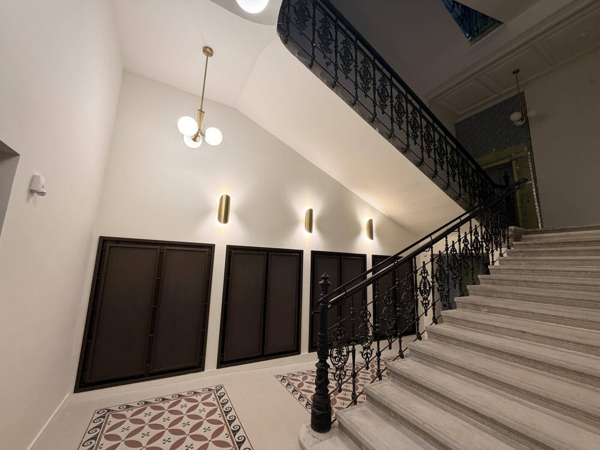 Elegantes Treppenhaus mit schmiedeeisernem Geländer, Marmorstufen und dekorativen Wandleuchten.