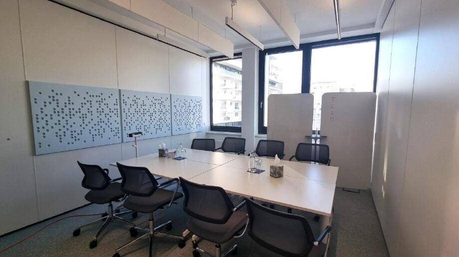 Moderner Konferenzraum mit großem Tisch, ergonomischen Stühlen und schallabsorbierenden Wandpaneelen für optimale Akustik.