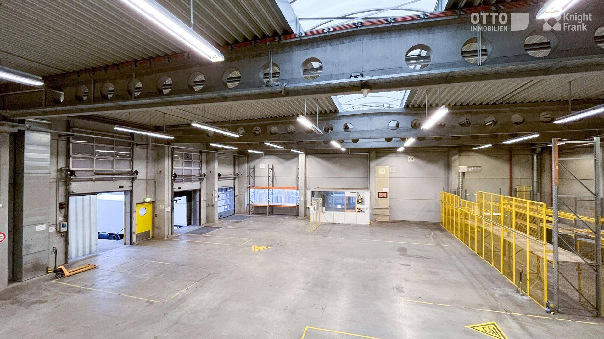 Geräumige Lagerhalle mit hohen Decken, Betonboden und mehreren Rolltoren für den Warenumschlag.