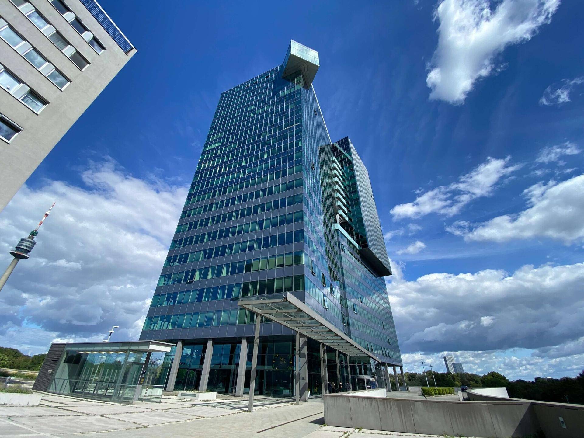 Beeindruckendes modernes Hochhaus mit Glasfassade unter blauem Himmel, umgeben von städtischer Infrastruktur.