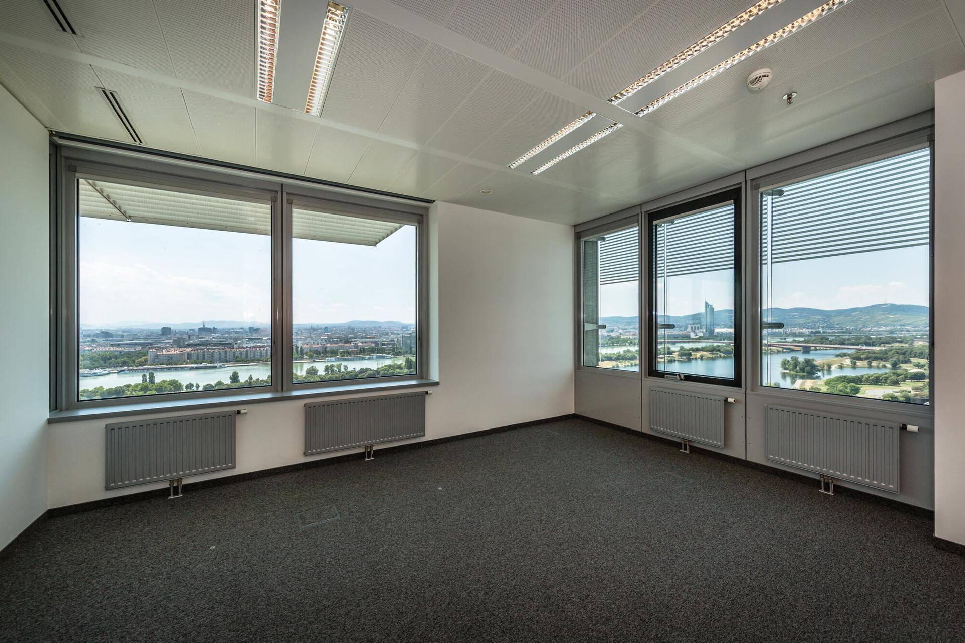 Leerer Büroraum mit Teppichboden und großen Fenstern, die einen weiten Blick auf die Stadt und den Fluss bieten.