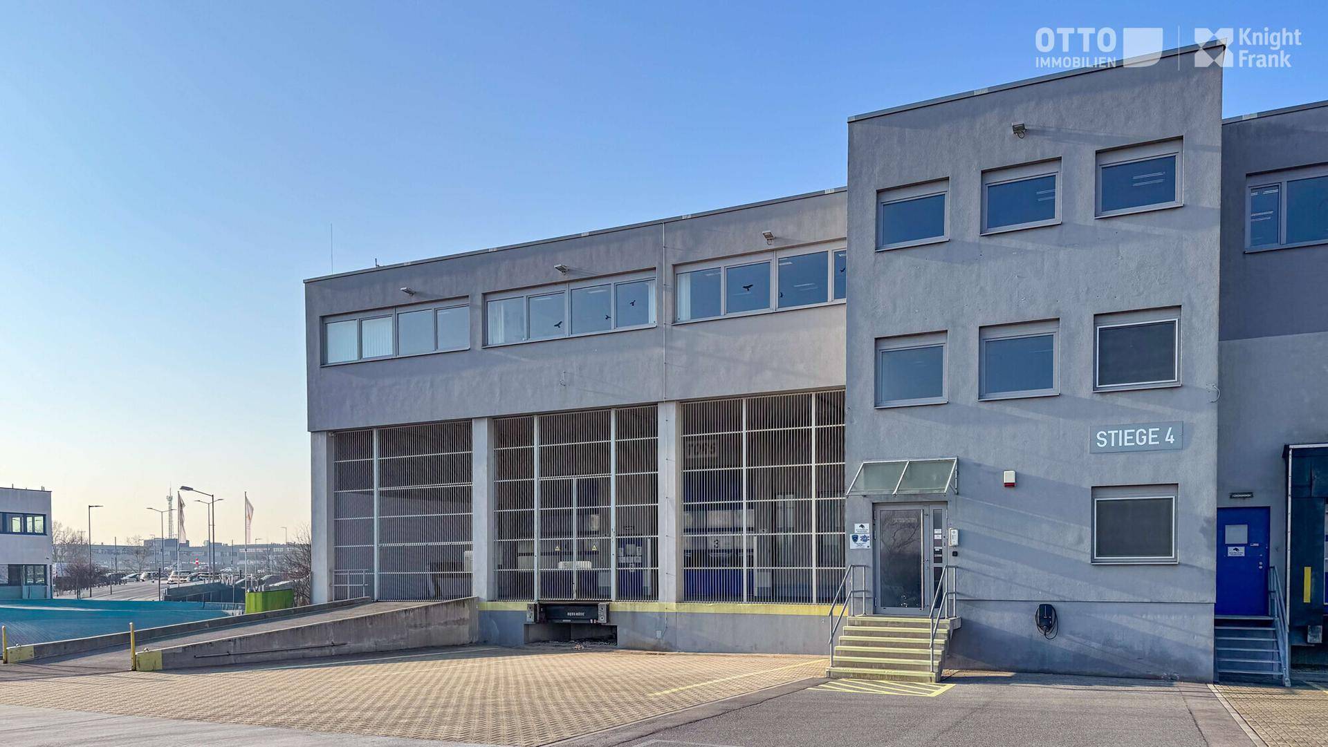 Außenansicht des Industriegebäudes mit Zufahrtsrampe und Eingangsbereich unter klarem Himmel.