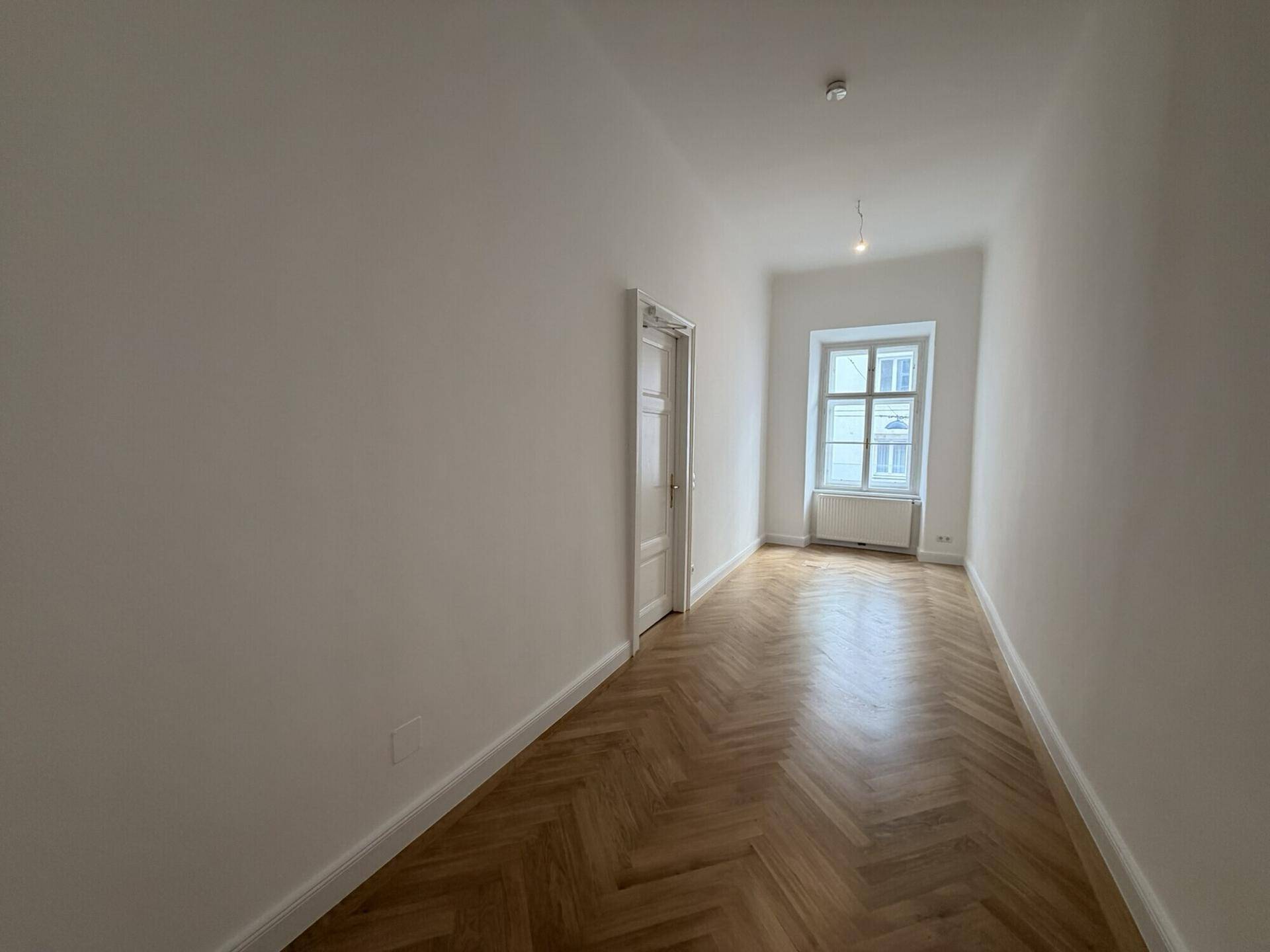 Gemütliches Zimmer mit Fischgrätparkett und einem Fenster, das den Raum mit natürlichem Licht versorgt.
