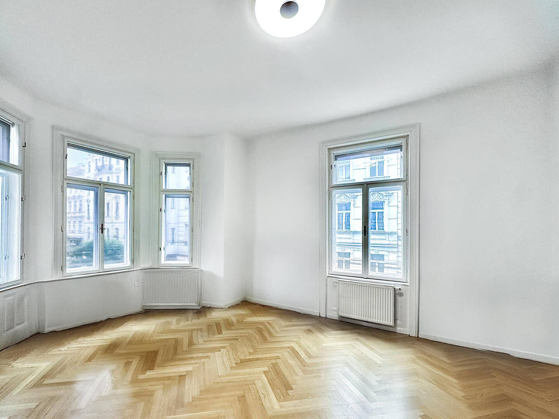 Geräumiges Wohnzimmer mit Erkerfenster, Fischgrätparkett und viel Tageslicht.