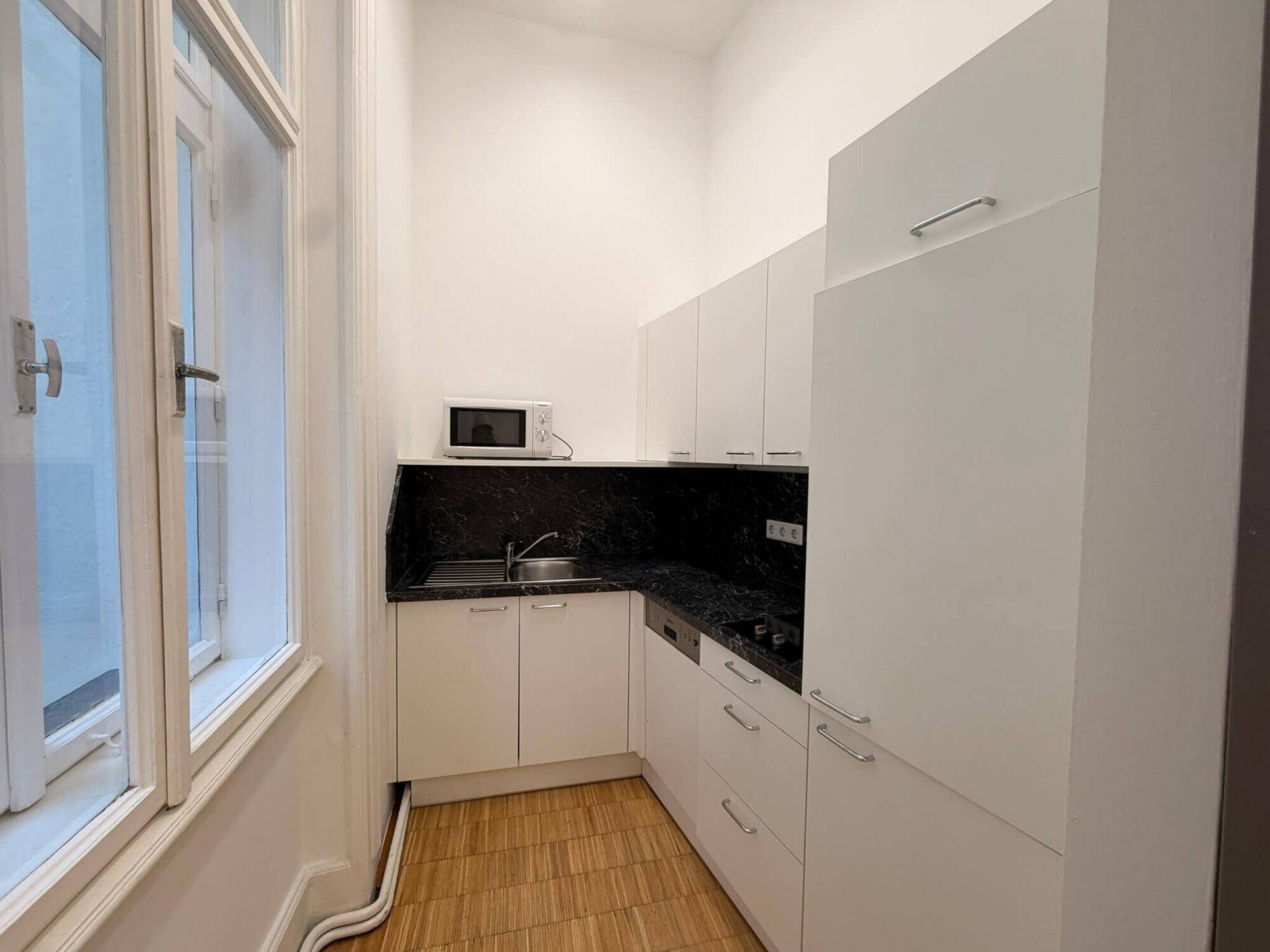 Funktionale Küchenzeile mit weißen Schränken, schwarzer Arbeitsplatte und Fenster, ausgestattet mit Mikrowelle und Geschirrspüler.