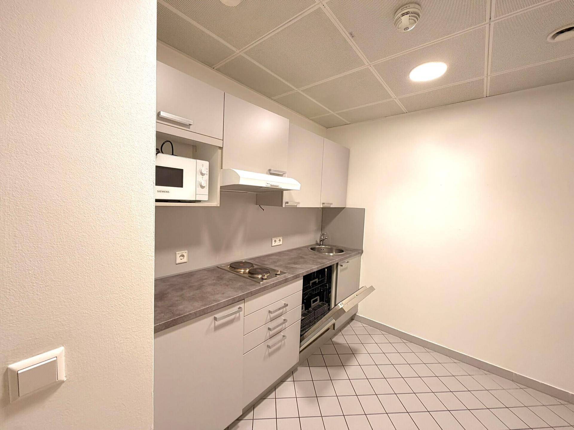 Kleine, funktionale Küchenzeile mit Mikrowelle, Kochfeld und Geschirrspüler, ideal für Büroräume.