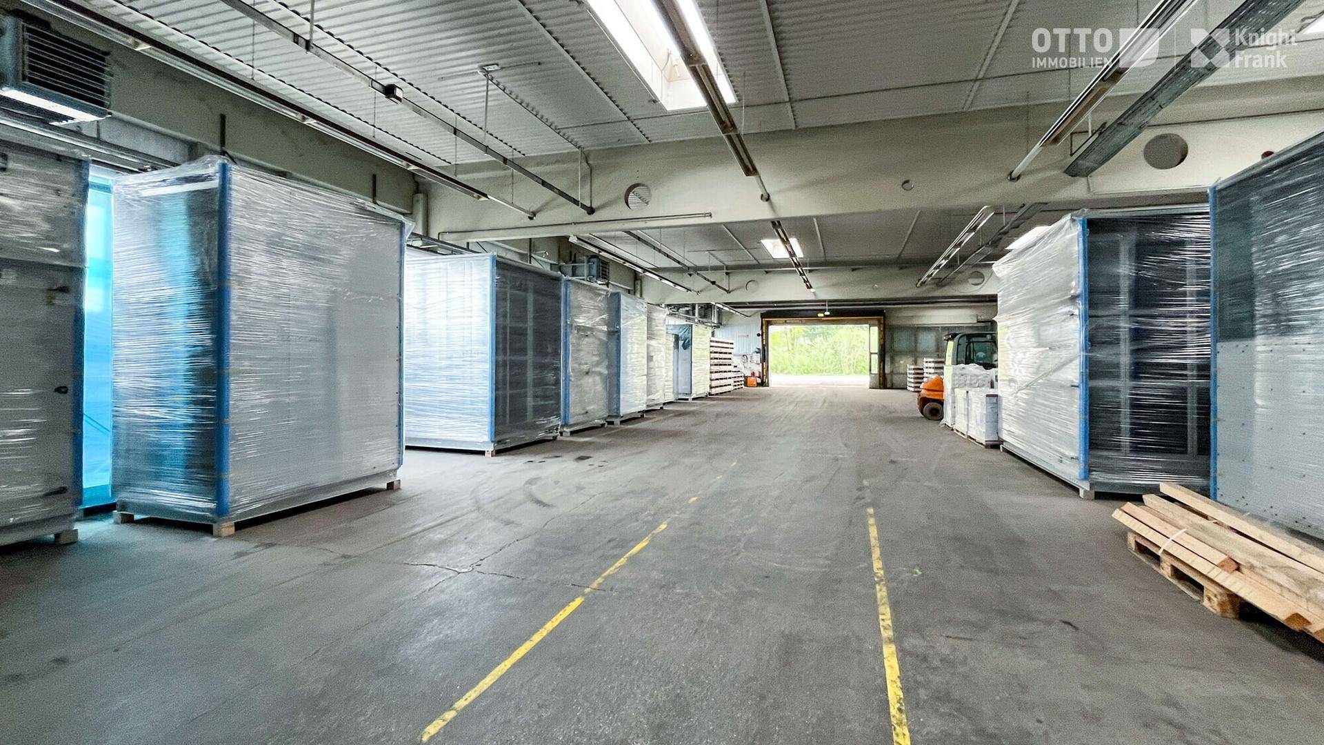 Innenansicht einer Lagerhalle mit verpackten Waren, Gabelstapler und Oberlichtern für Tageslicht.
