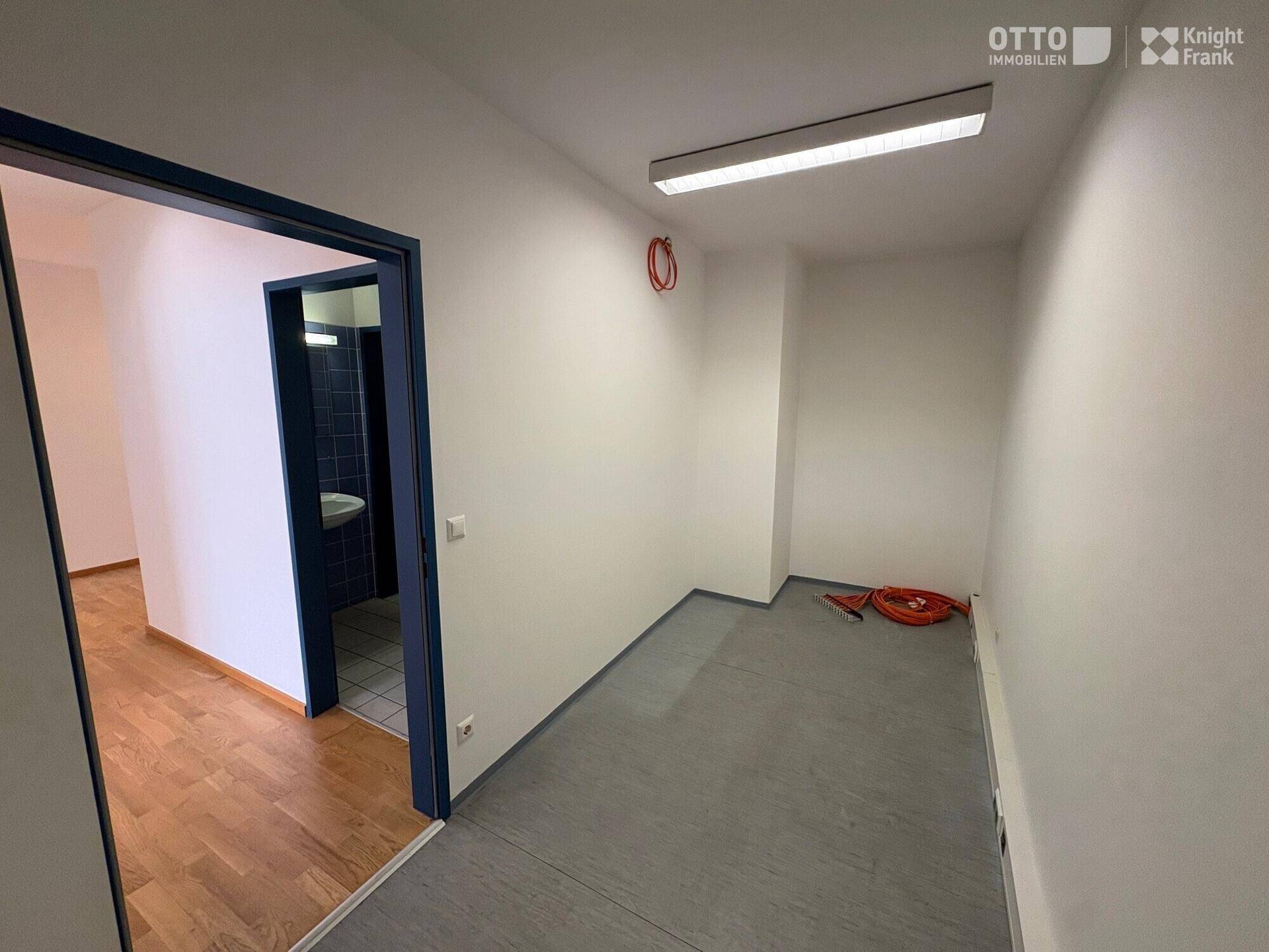Kleiner Büroraum mit grauem Vinylboden und Zugang zu einem gefliesten Badezimmer.
