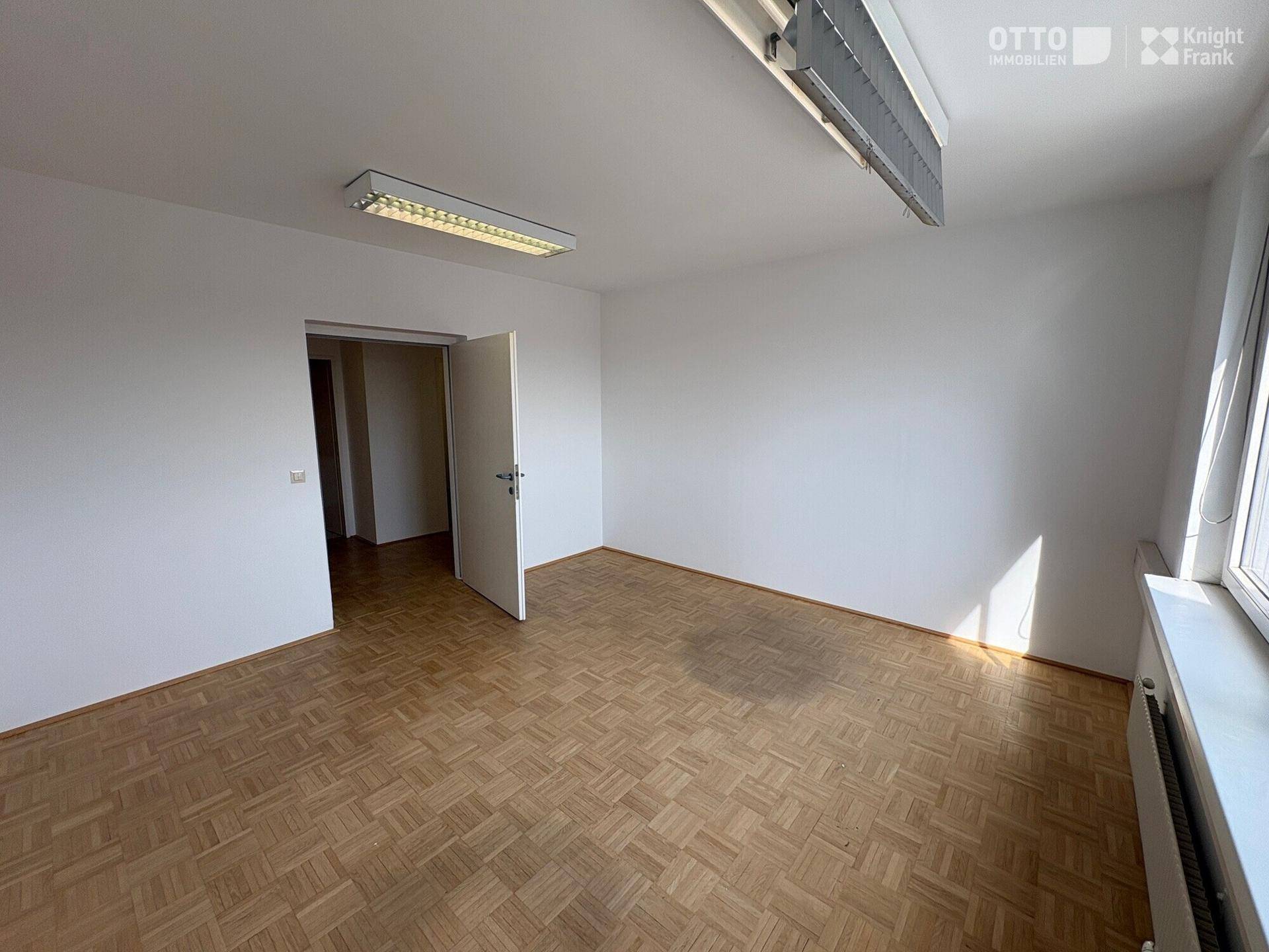 Geräumiges Büro mit Parkettboden und großen Fenstern, die für eine helle und offene Arbeitsumgebung sorgen.