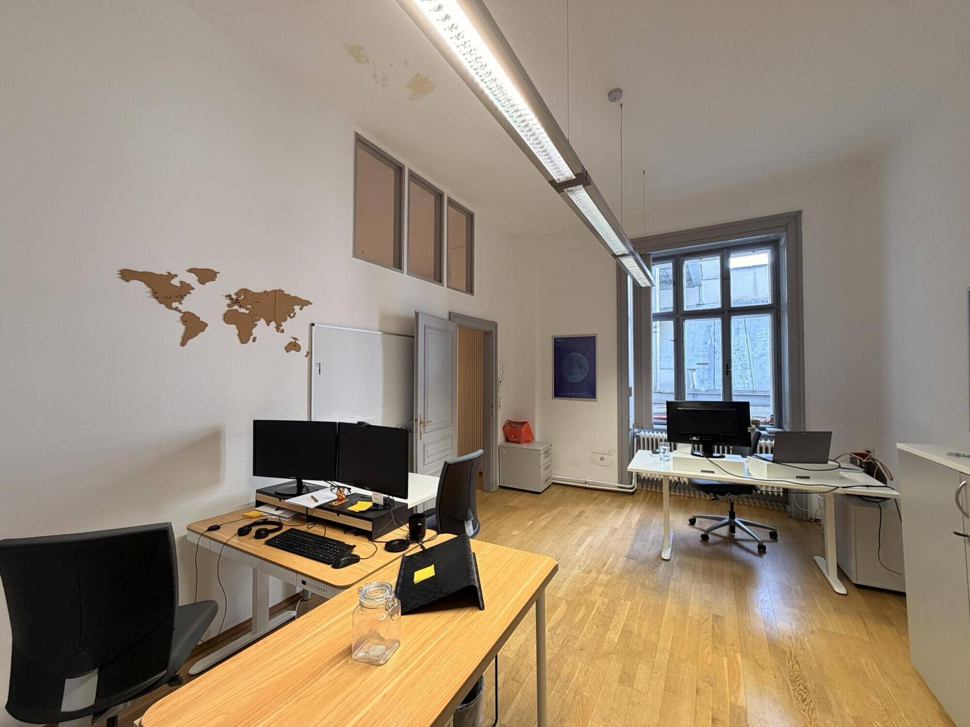 Helles Büro mit mehreren Arbeitsplätzen, Holzboden und einem großen Fenster mit Blick nach draußen.