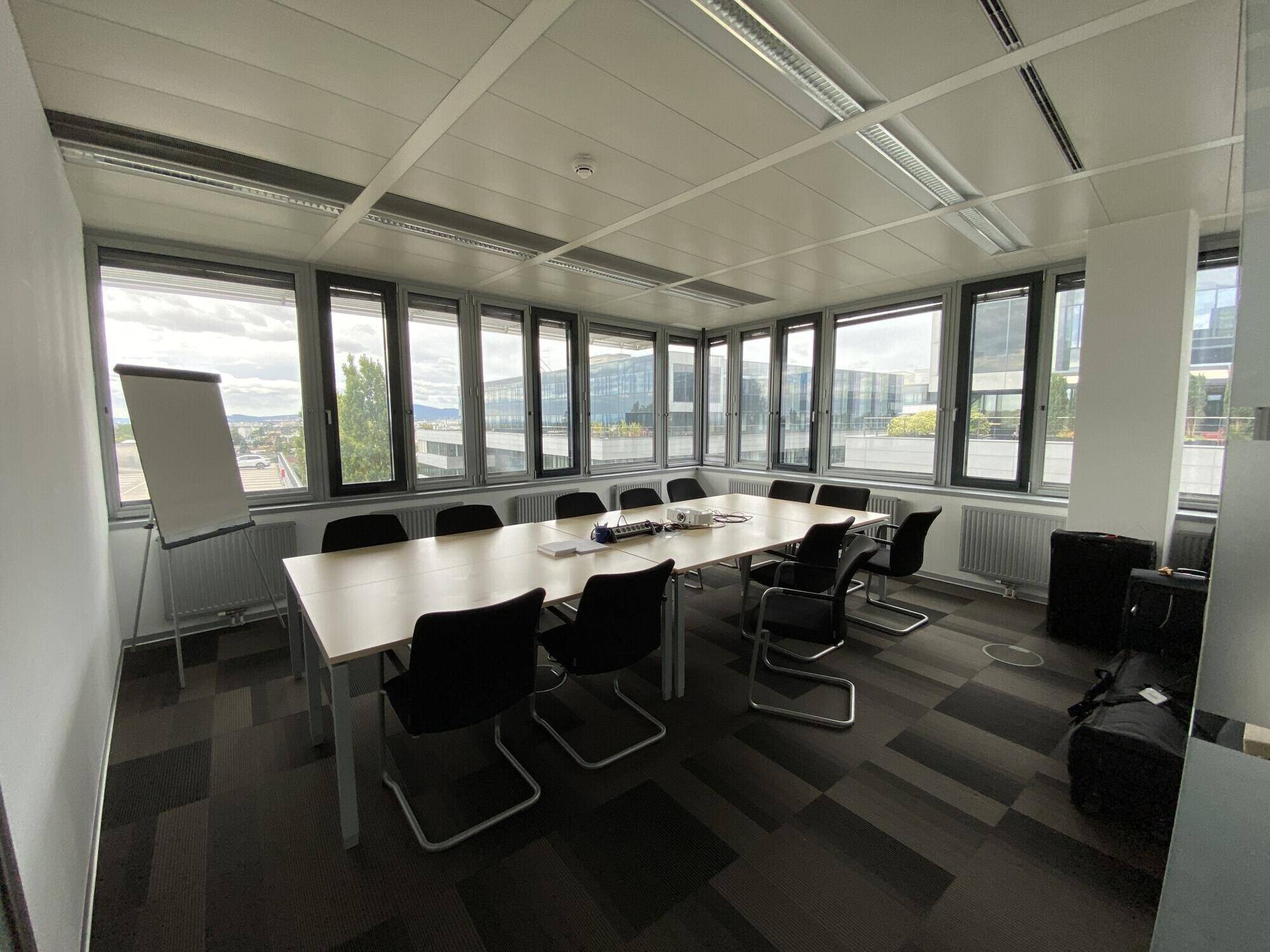 Großer Konferenzraum mit langem Tisch, vielen Stühlen und umlaufenden Fenstern mit Stadtblick.