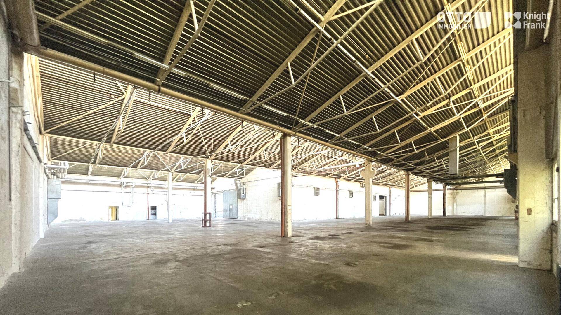 Weitläufige Industriehalle mit markanter Dachkonstruktion und vielen Stützpfeilern.