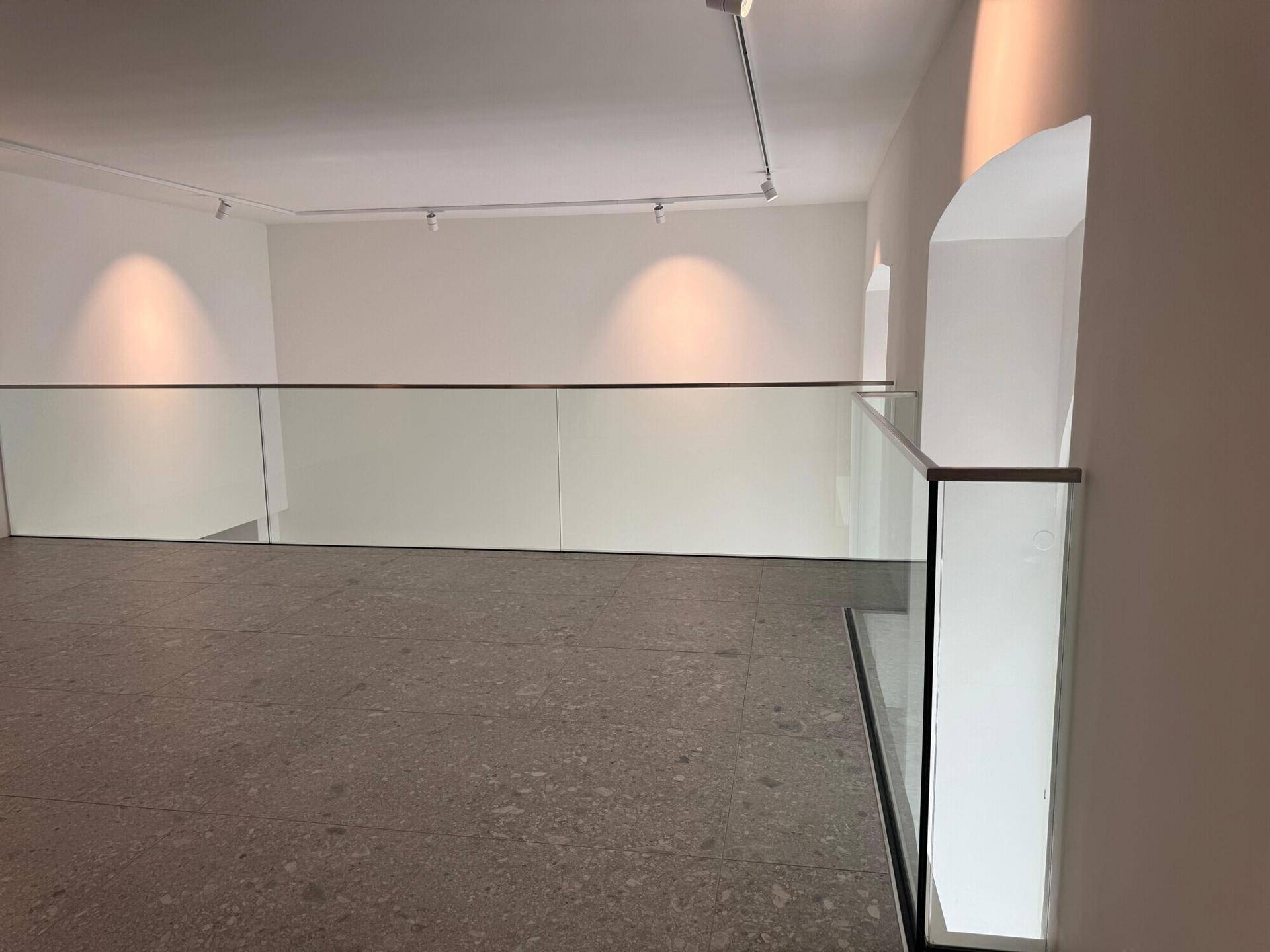 Die moderne Galerie mit Glasgeländer bietet einen offenen Blick in den darunterliegenden Gewerberaum und betont das luftige Design.