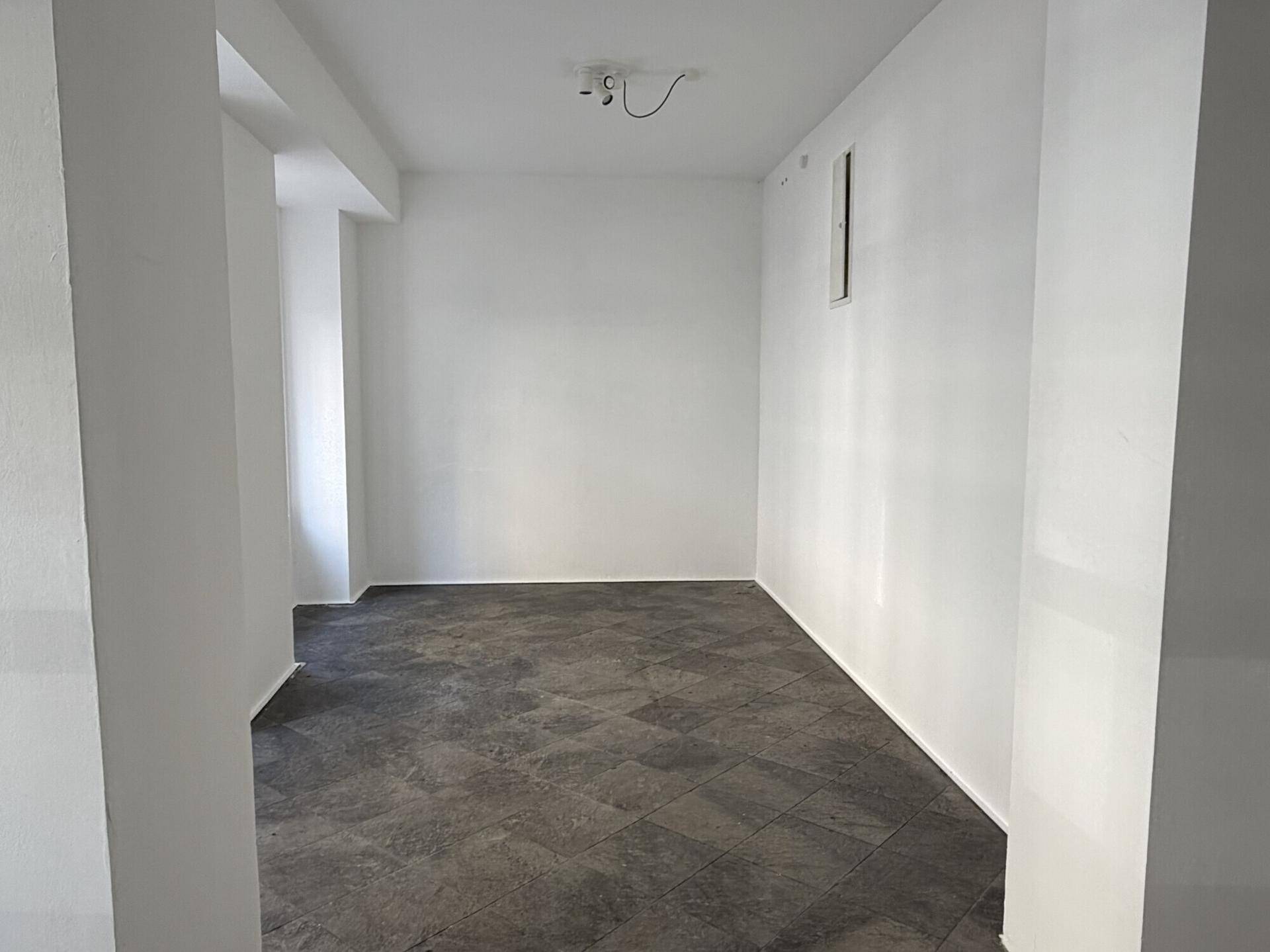 Schmaler, leerer Raum mit dunklem Fliesenboden und weißen Wänden, ideal für verschiedene Nutzungen.