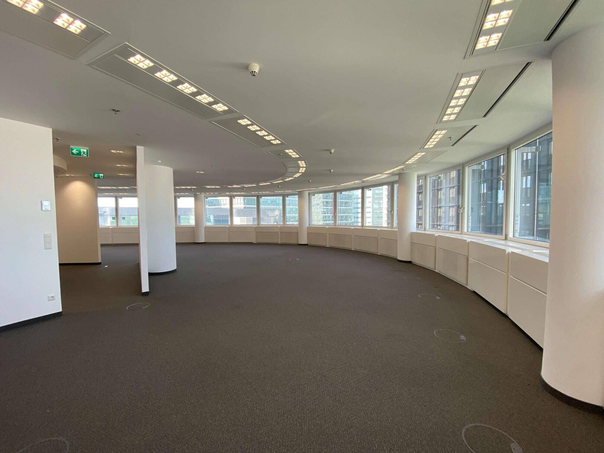 Weitläufiger Bürobereich mit Teppichboden und einer geschwungenen Fensterfront, die einen Panoramablick bietet.
