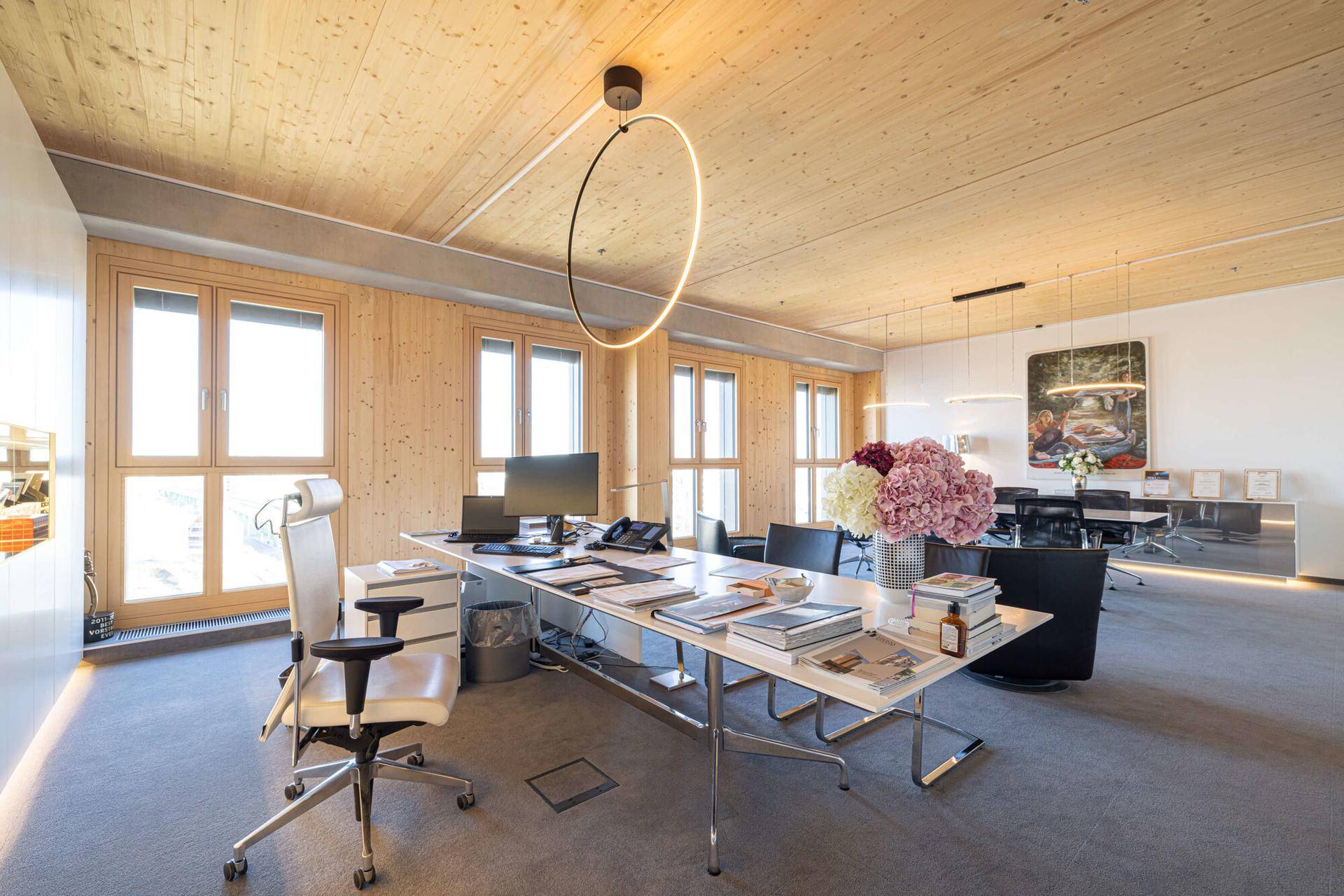 Helles, modernes Büro mit Holzwänden und -decke, großen Fenstern und Teppichboden.