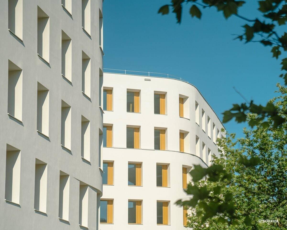 Detailansicht eines modernen weißen Gebäudes mit abgerundeter Ecke und vielen Fenstern.